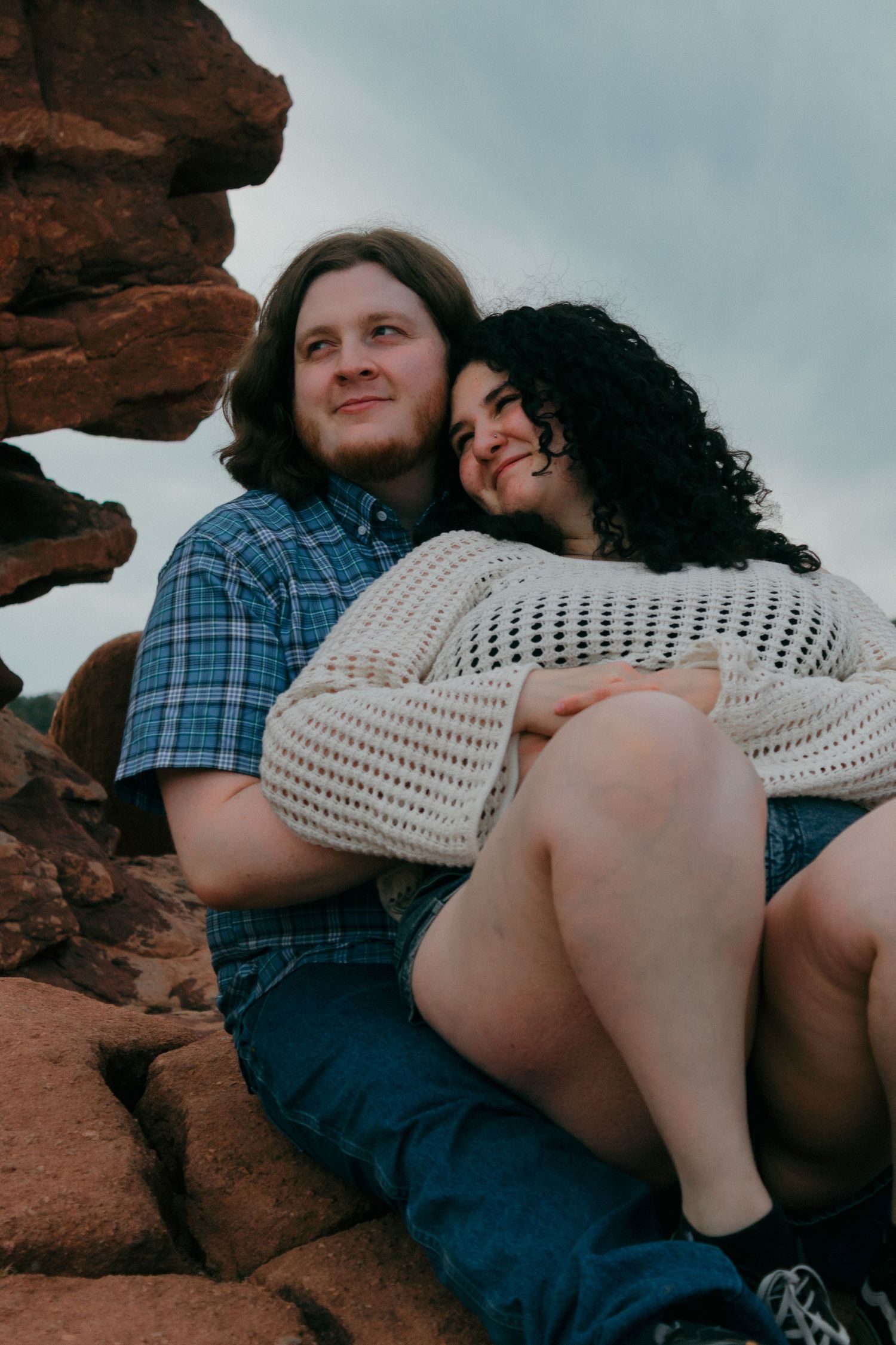 Candid moment shared between couple resting against desert rock formations.