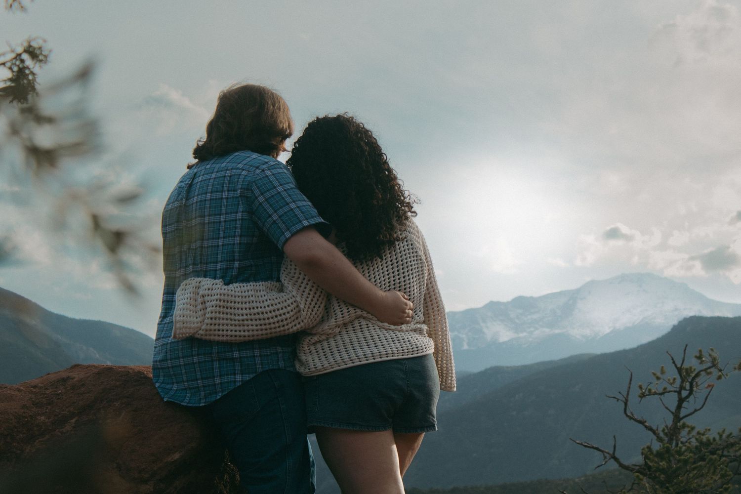 Two people share a tender moment while looking out at a misty mountain vista.