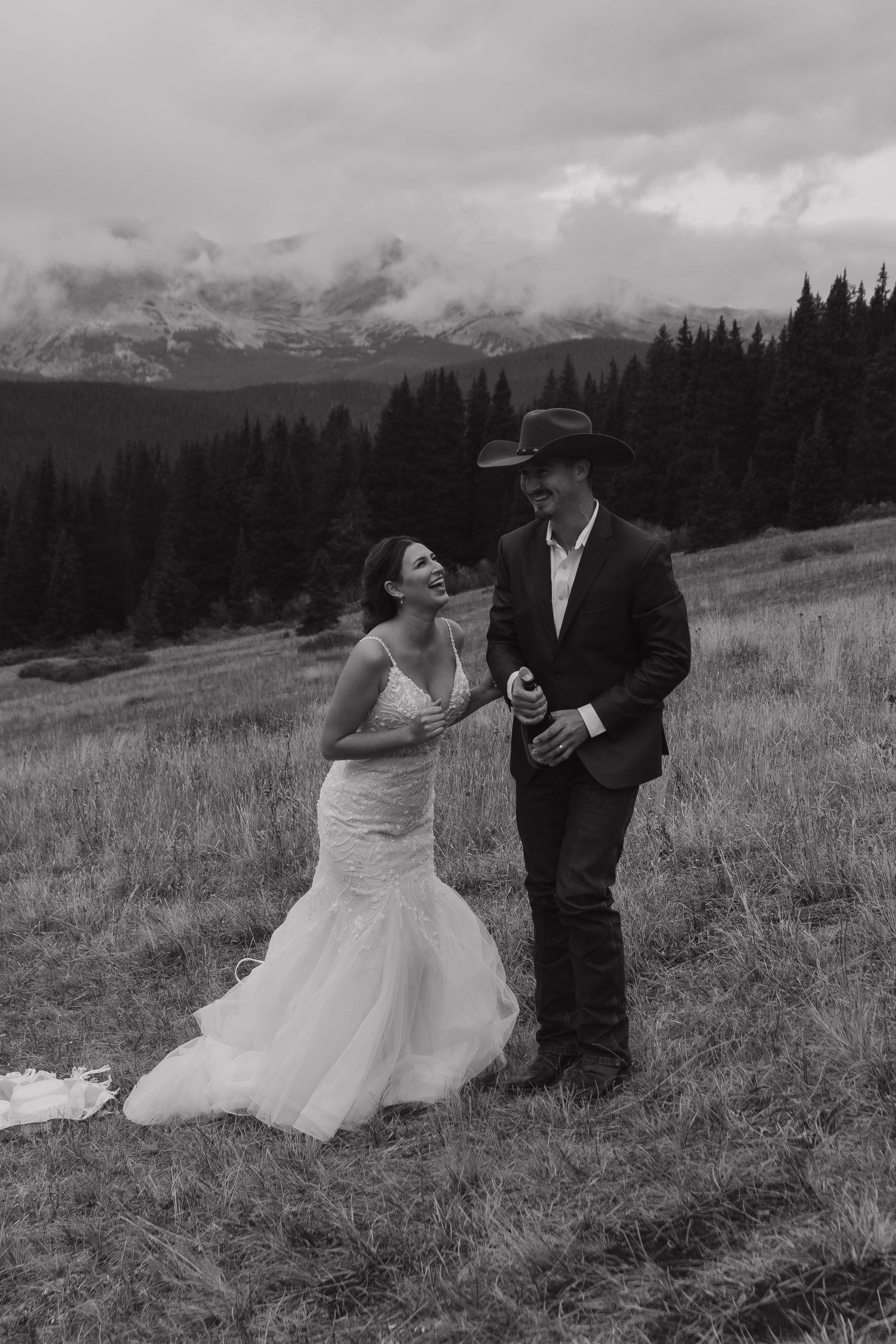 A couple dances together in a mountain meadow with forest and peaks in the background.