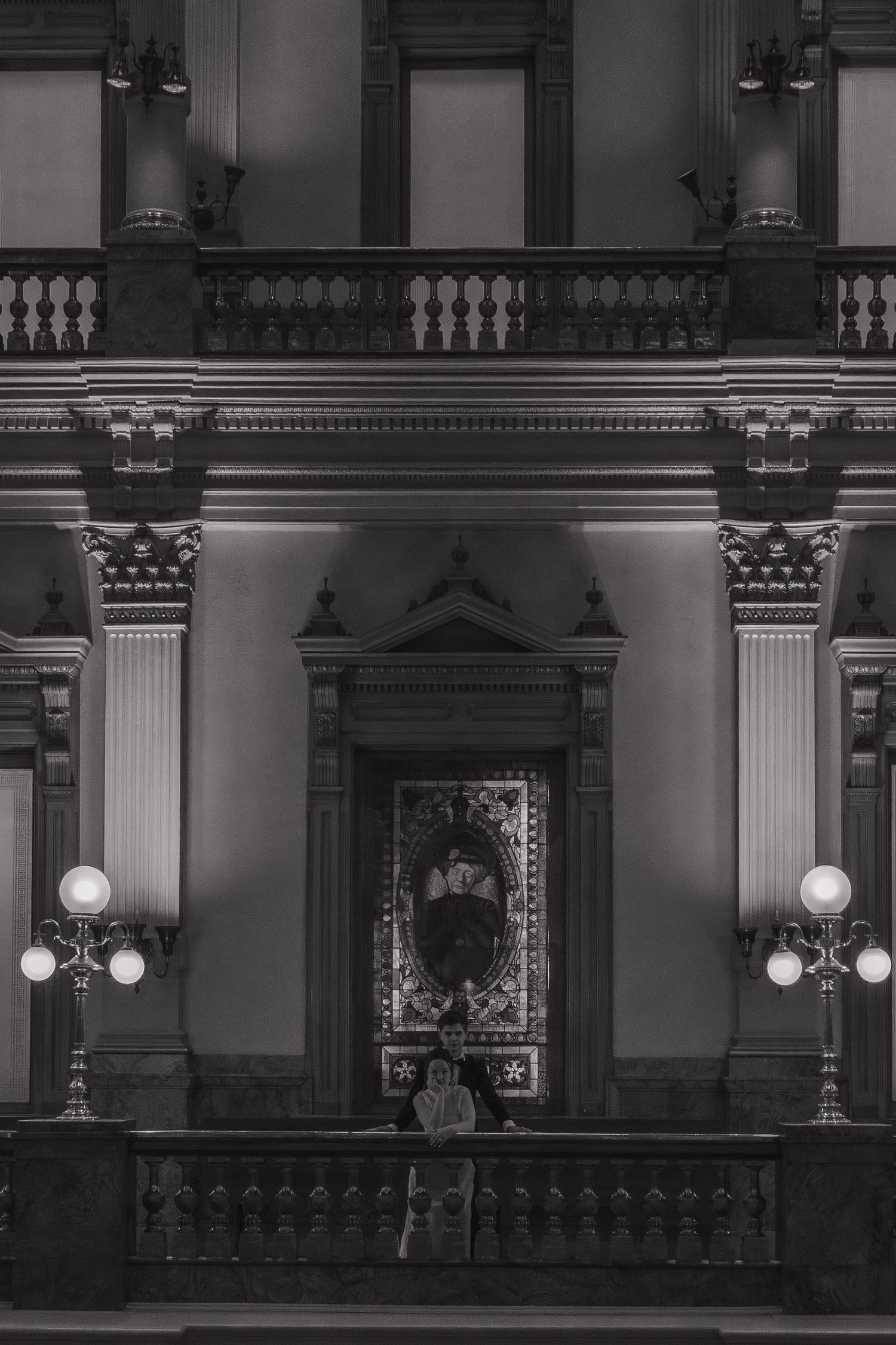 A dramatic black and white architectural shot of a grand interior with columns and ornate lighting fixtures.