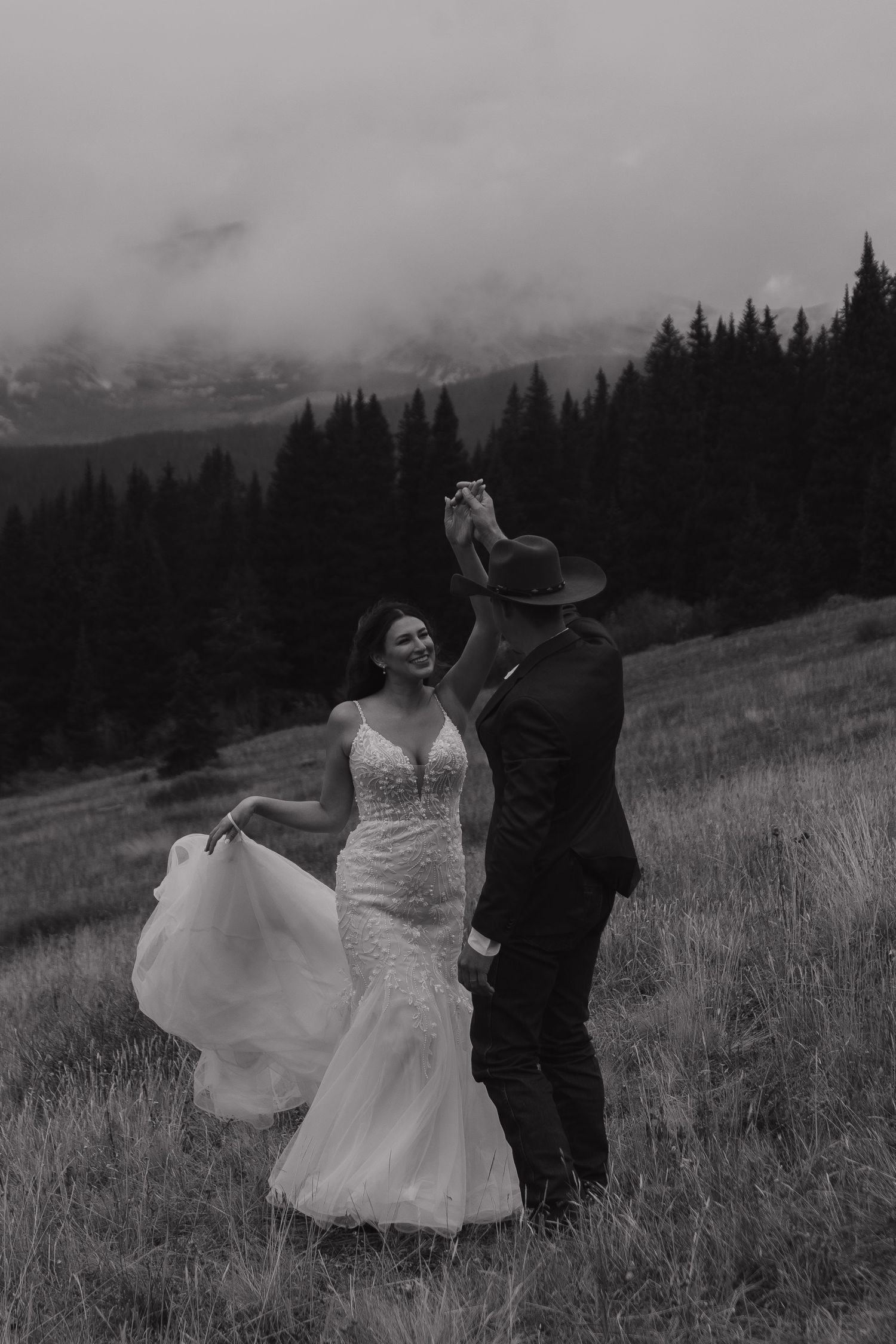 A couple dances together on a misty mountainside meadow with evergreen trees in the background.