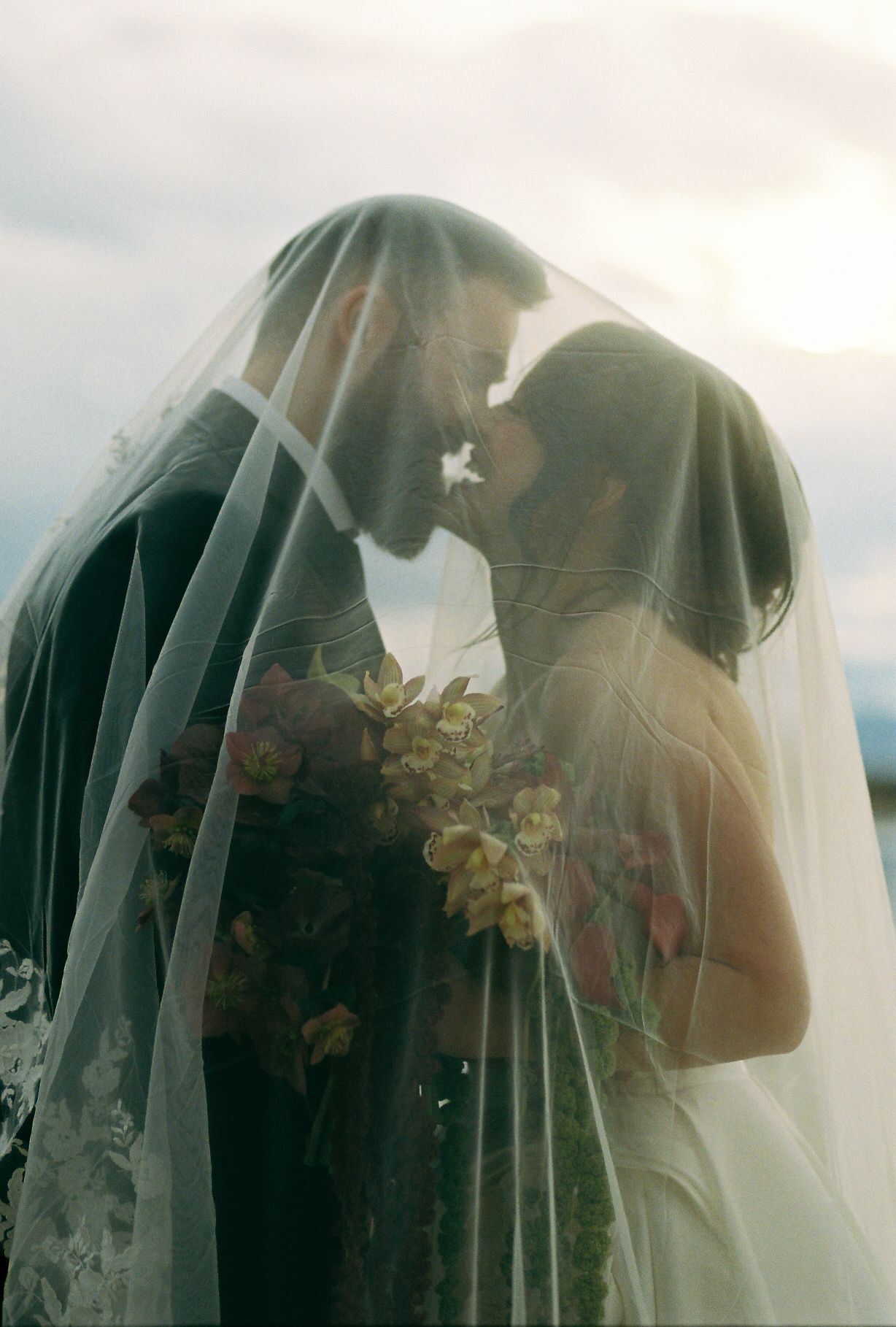 A romantic wedding moment captured through a delicate veil during sunset.