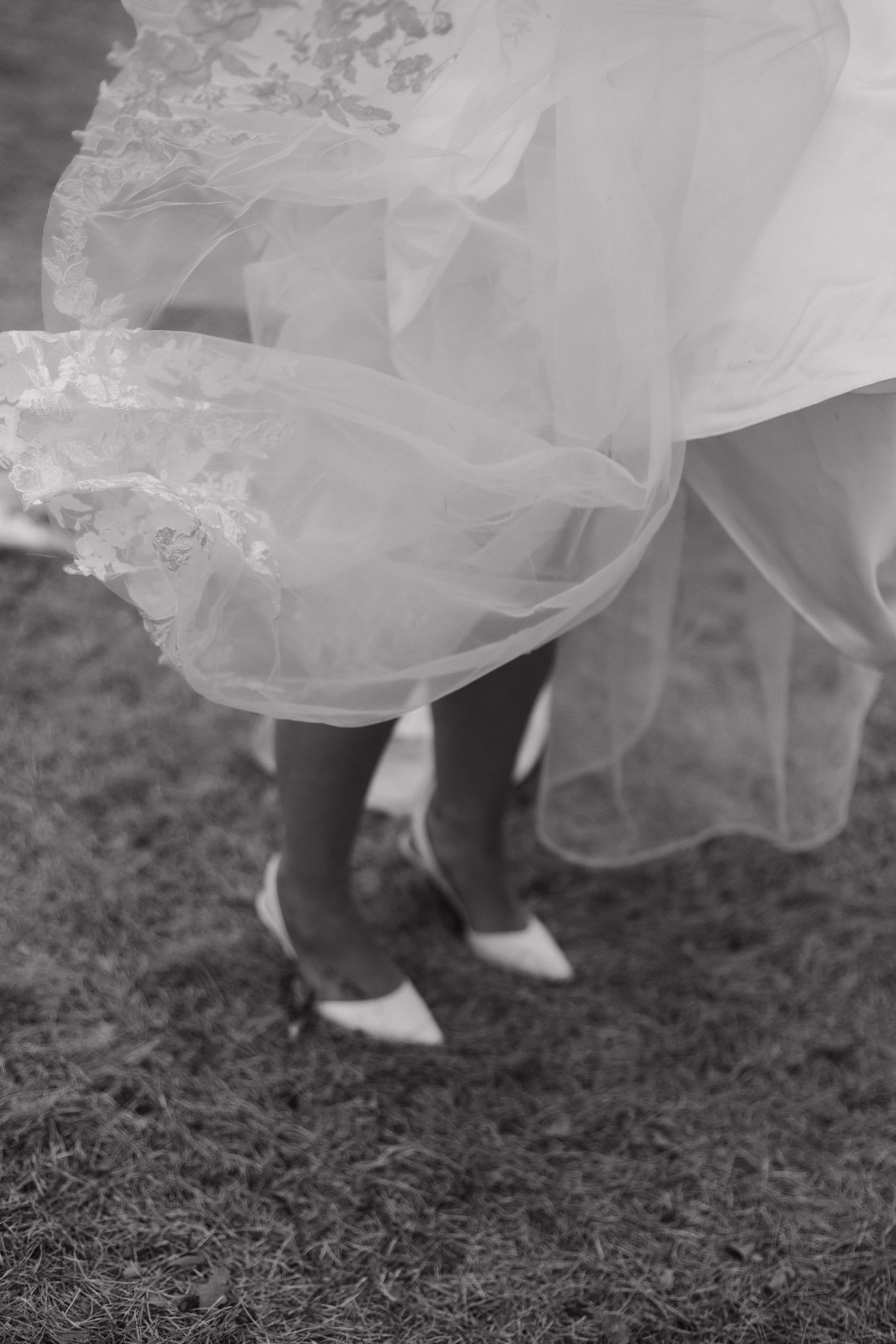 The hem of a flowing white wedding dress brushes against dark ground.