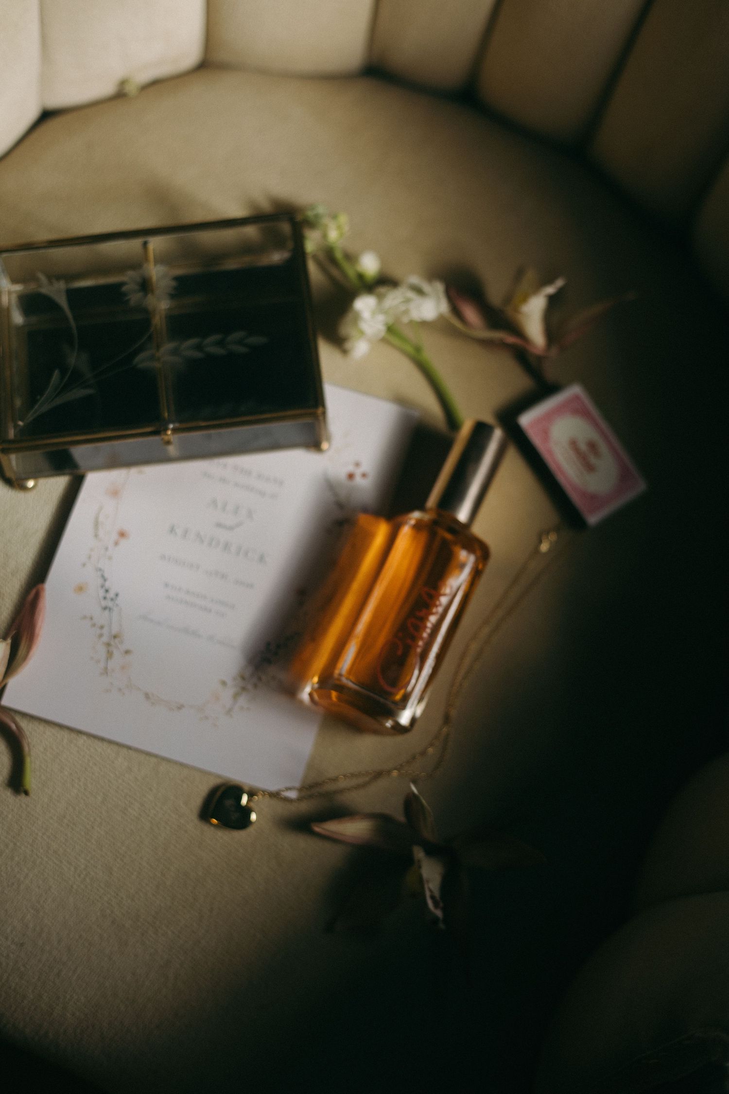 Wedding details including an invitation, perfume bottle, and flowers on a textured surface.