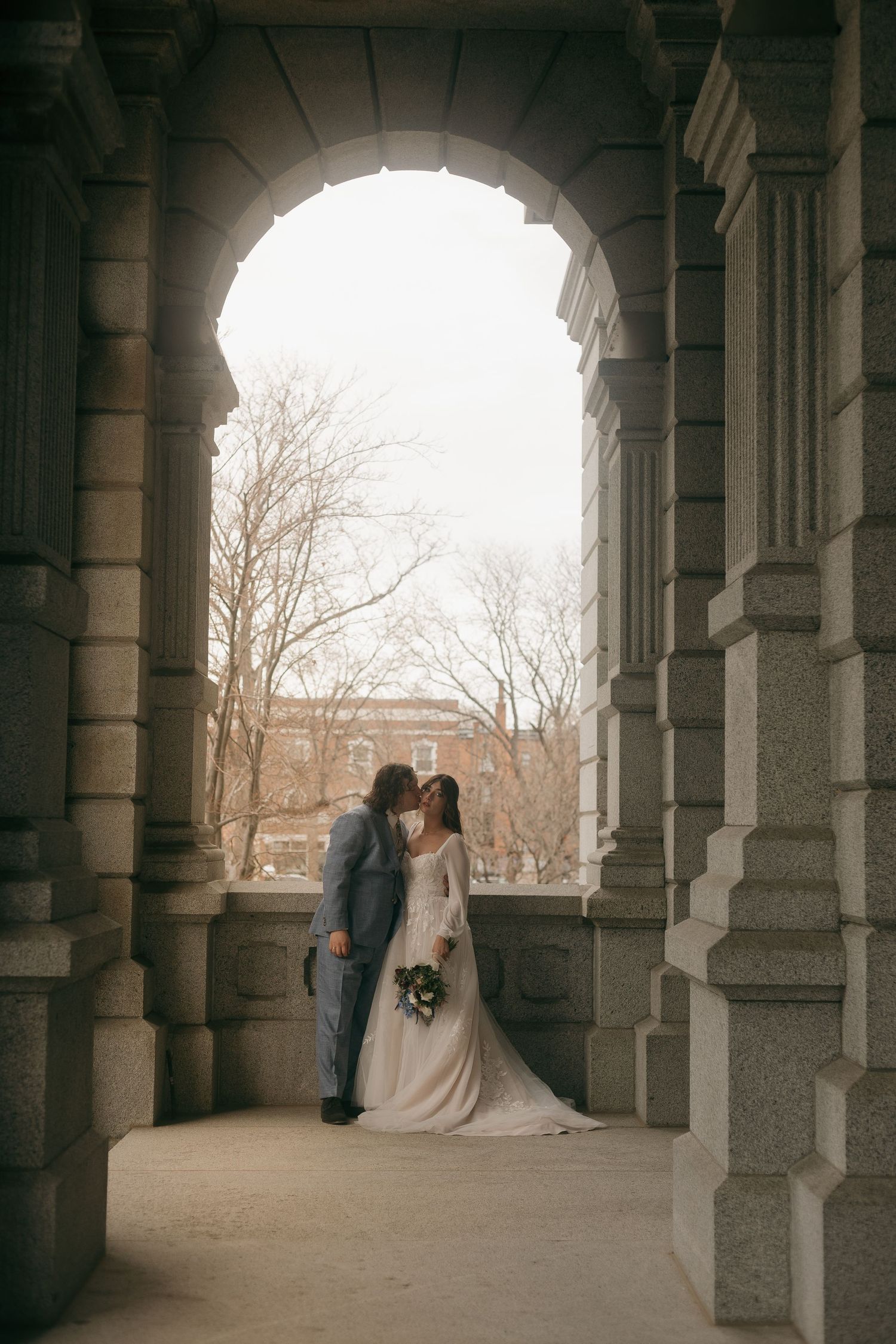 Newlyweds share an intimate moment under stone archways of historic building.