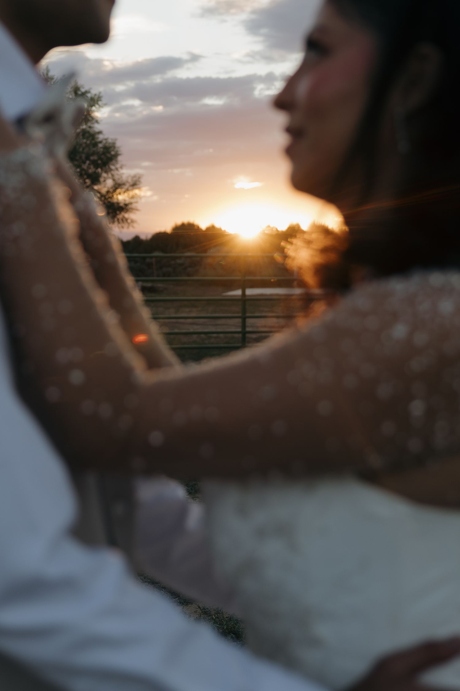 Blurred artistic shot of bride and groom embracing with golden sunset in background.