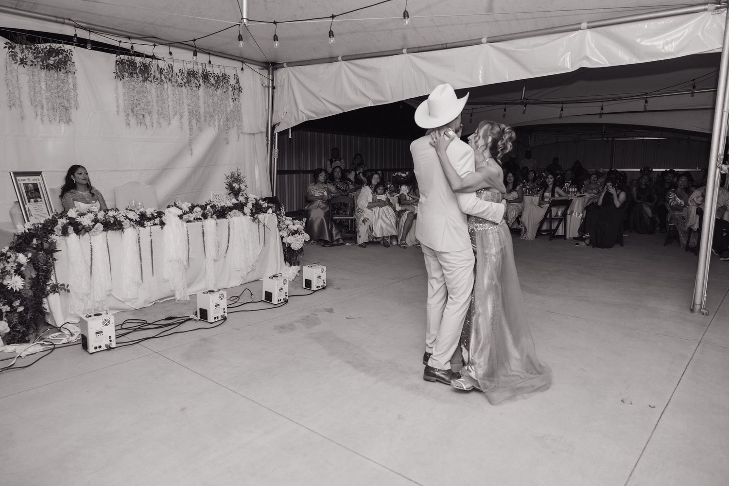 A couple shares their first dance under a tent at a rustic wedding reception in black and white.