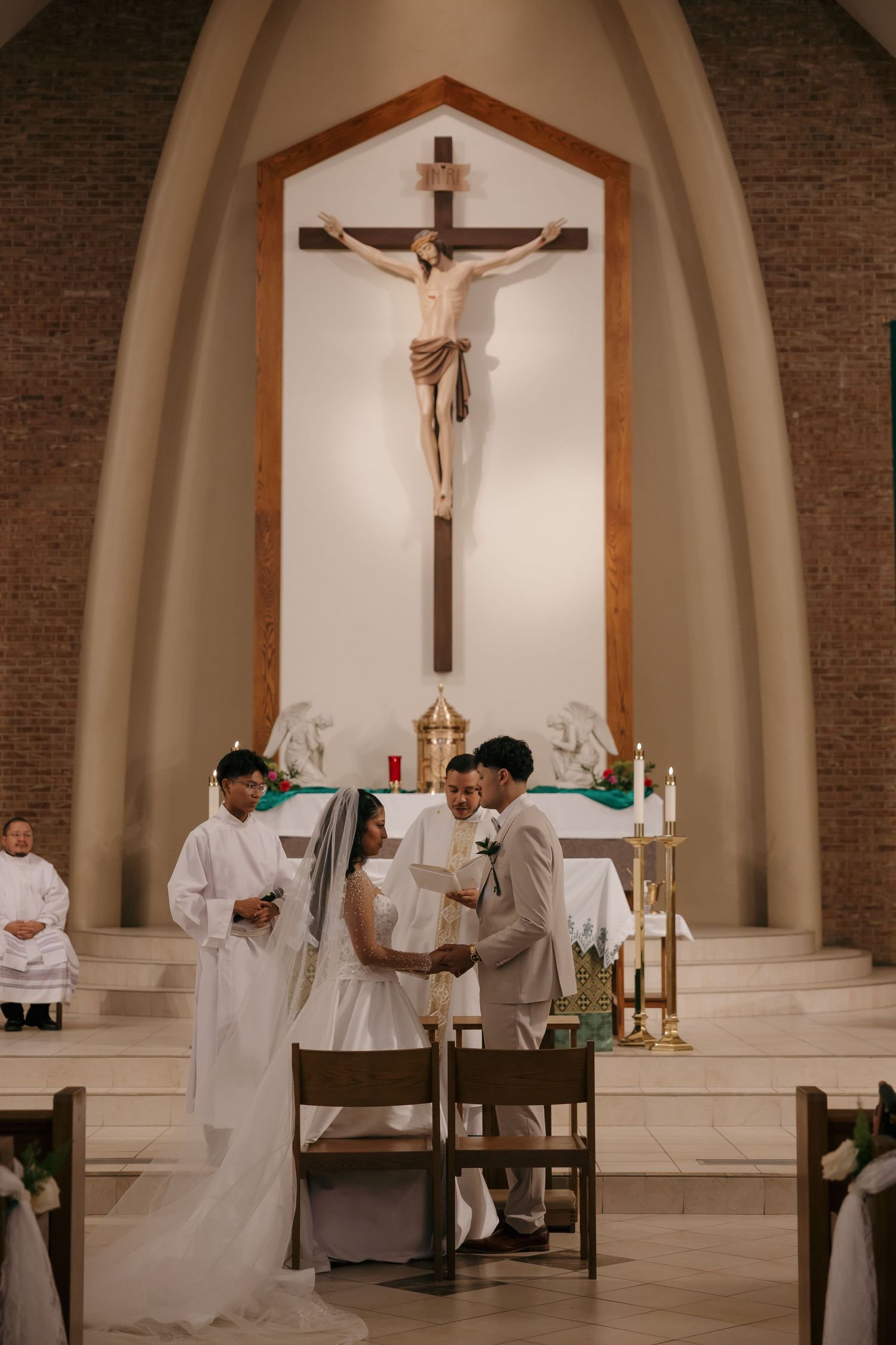 Bride and groom exchange vows at Catholic church altar with crucifix backdrop during wedding ceremony.