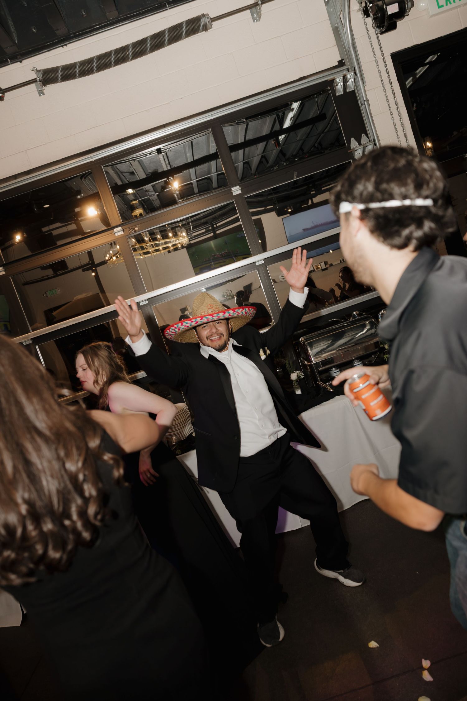 Wedding guest dancing in sombrero hat at lively indoor wedding reception celebration.