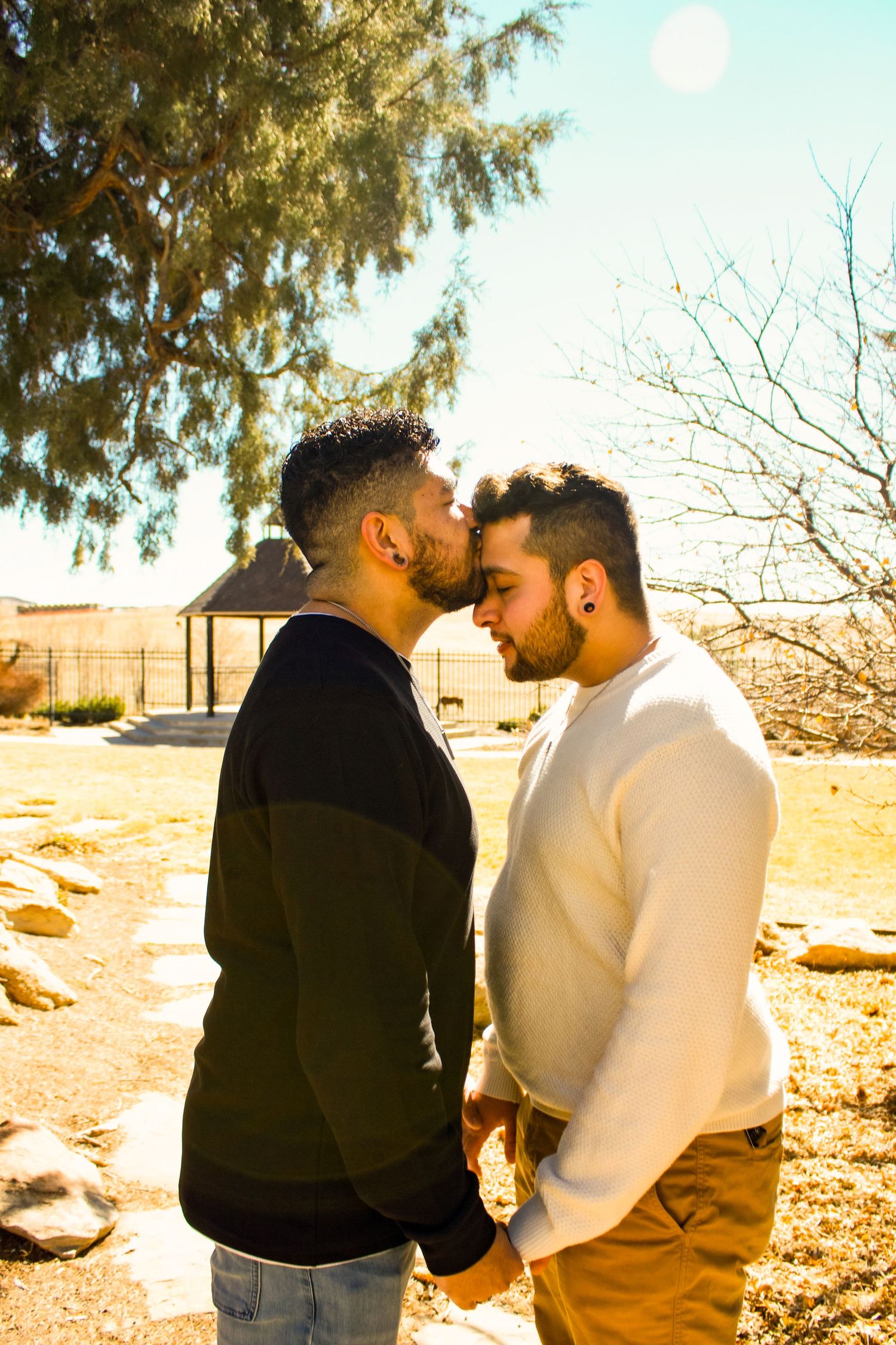 Two individuals share a tender embrace outdoors near a desert gazebo.