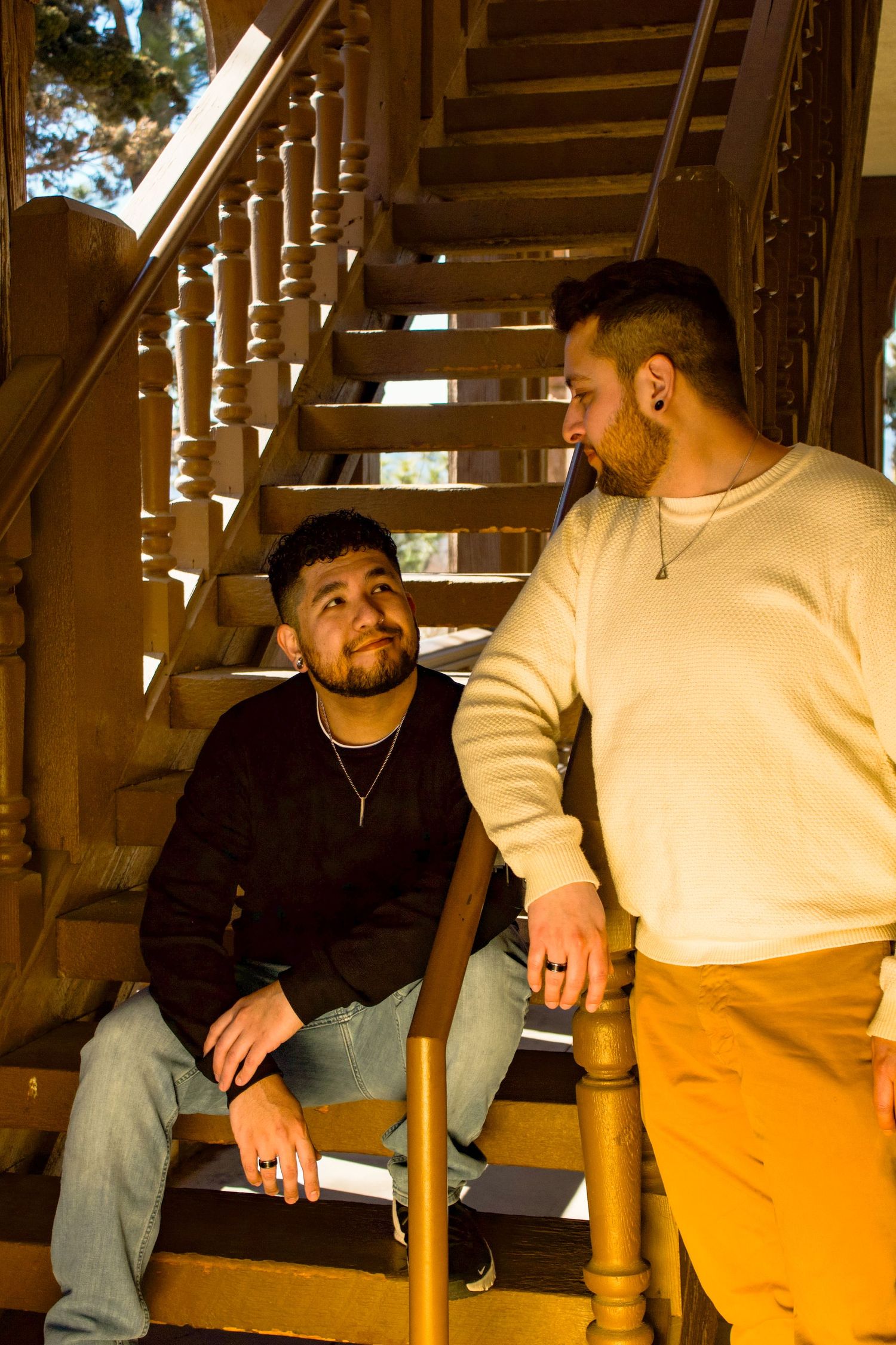 Two people sit close together on wooden stairs, engaged in conversation with natural lighting.