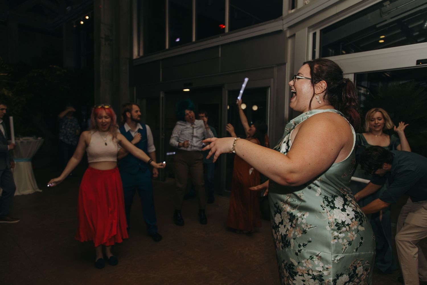 Guests dancing energetically at indoor wedding reception with colorful lighting and festive atmosphere.