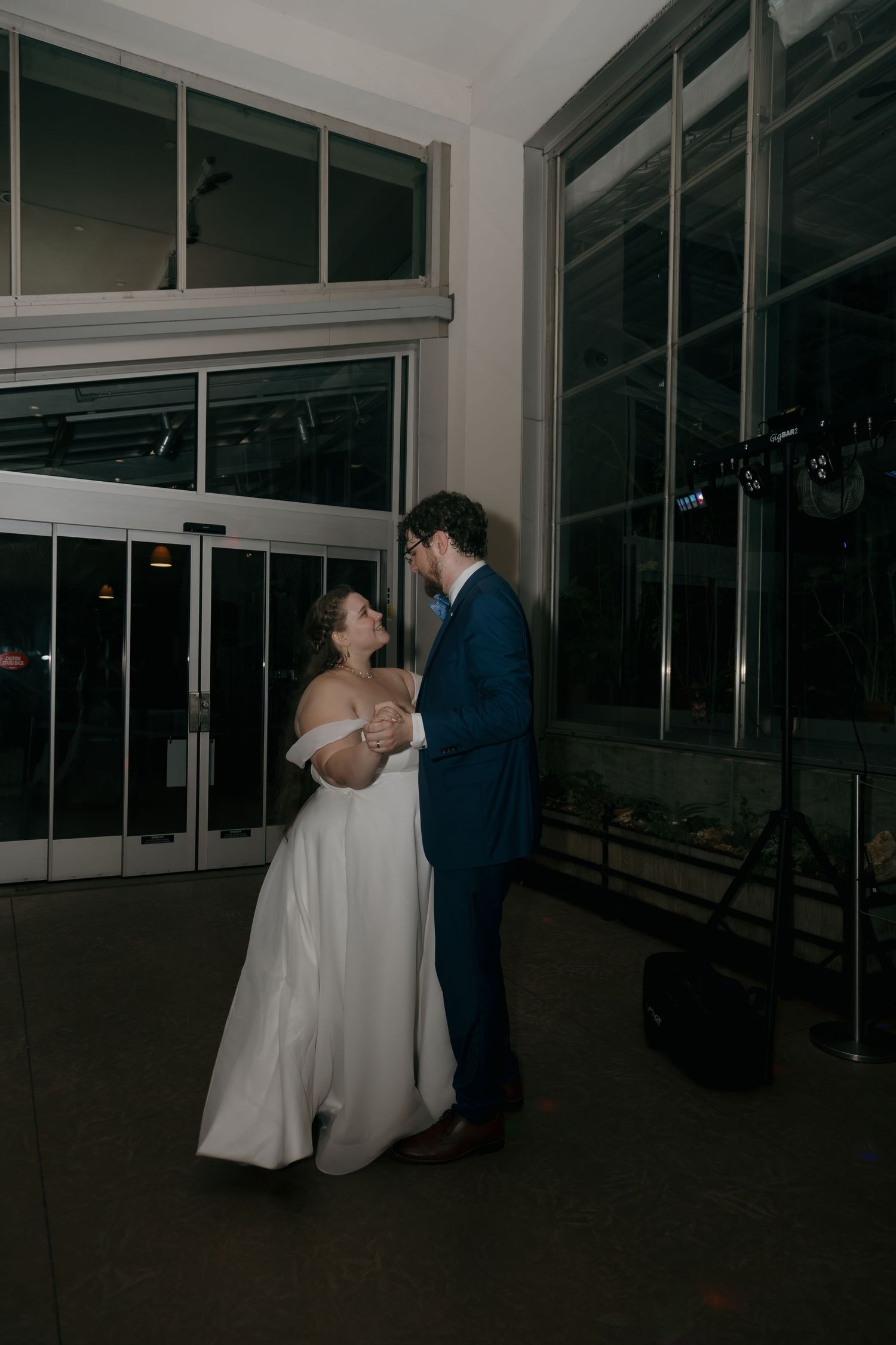 Bride and groom share first dance near large windows in elegant indoor wedding reception venue.