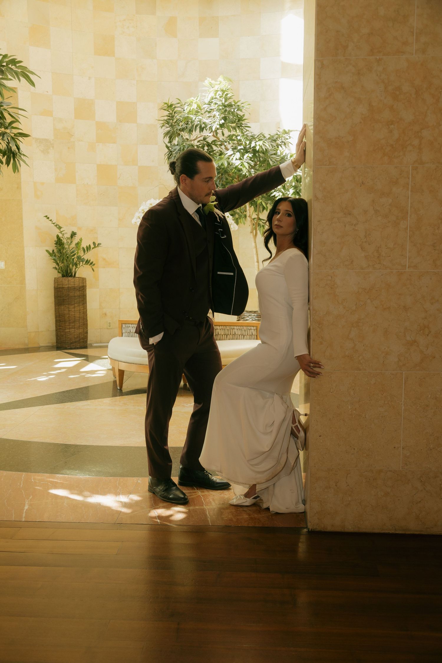 Bride in fitted white gown and groom in dark suit posing in elegant indoor venue.