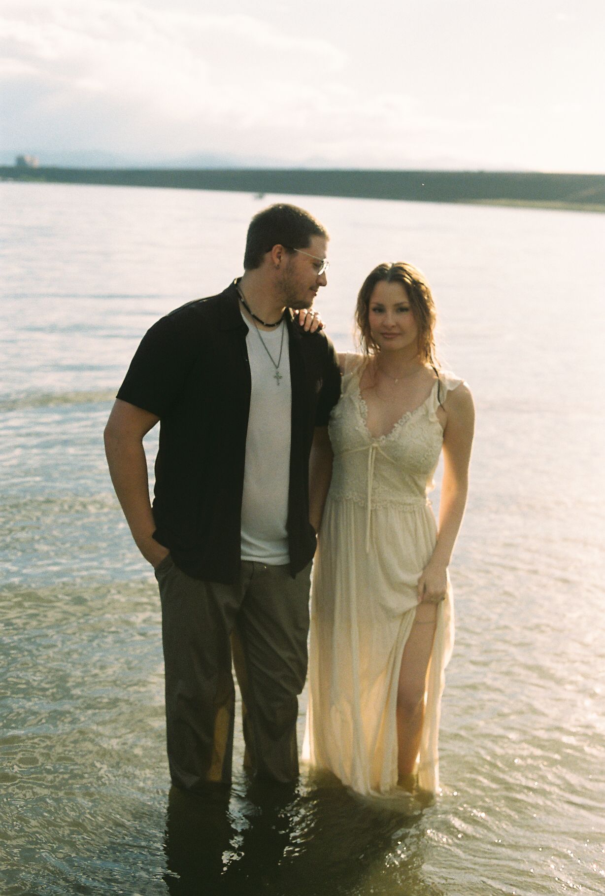 Smiling couple standing together in shallow lake water during golden hour.