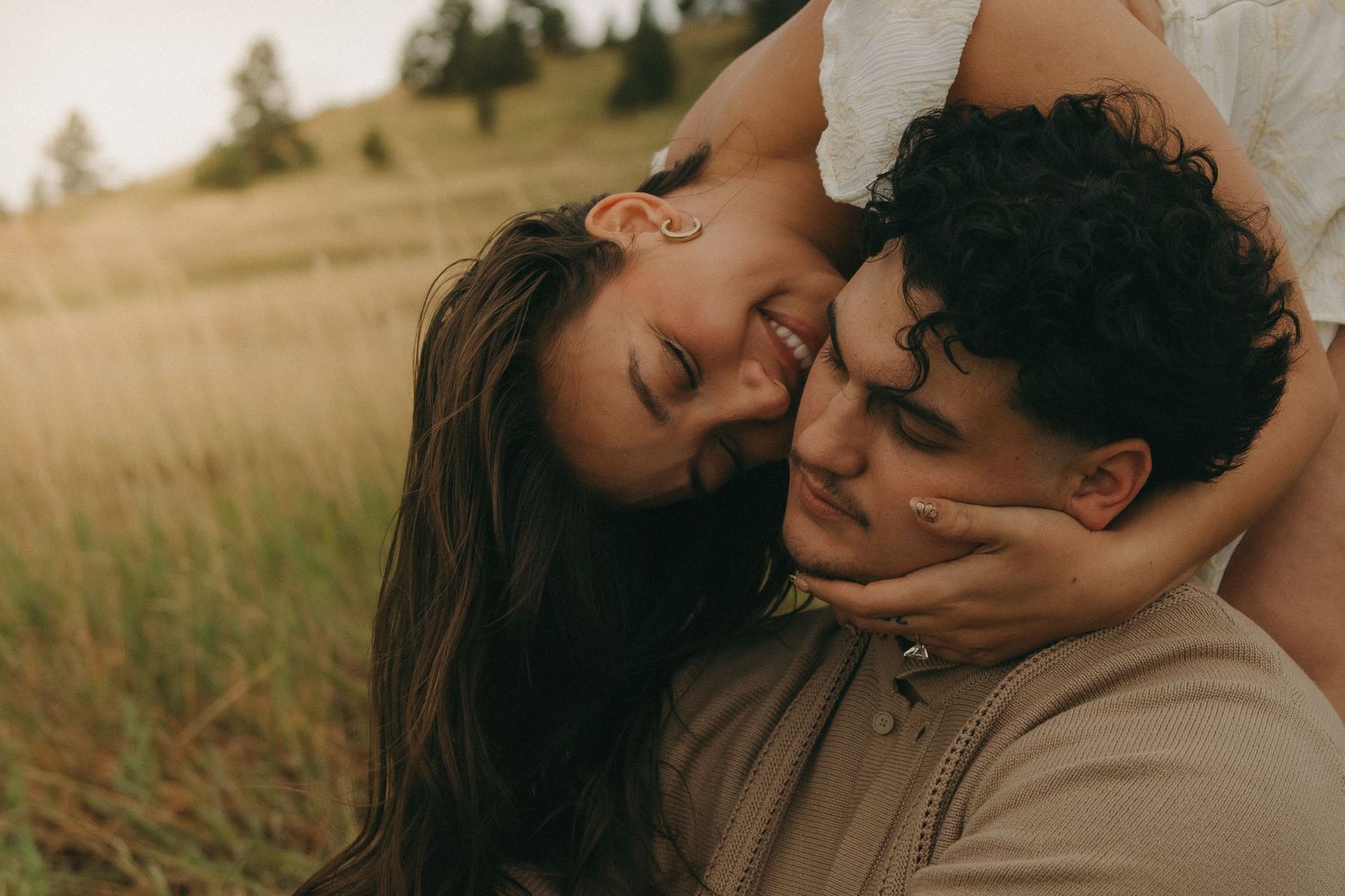Intimate close-up of couple smiling and cuddling together in a sunlit grassy meadow.