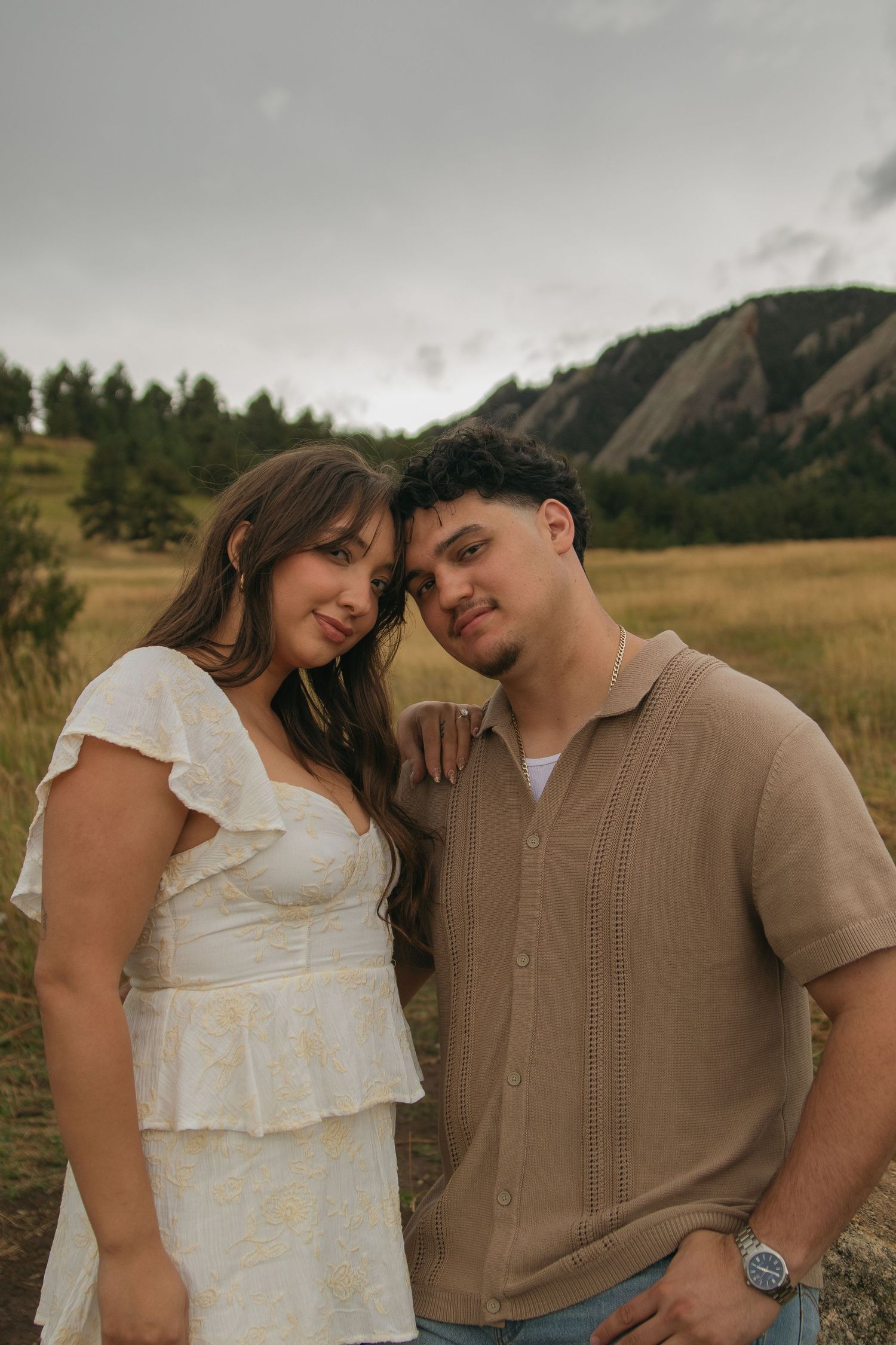 A couple poses together in a field with the Flatirons mountains visible behind them in Boulder, CO.