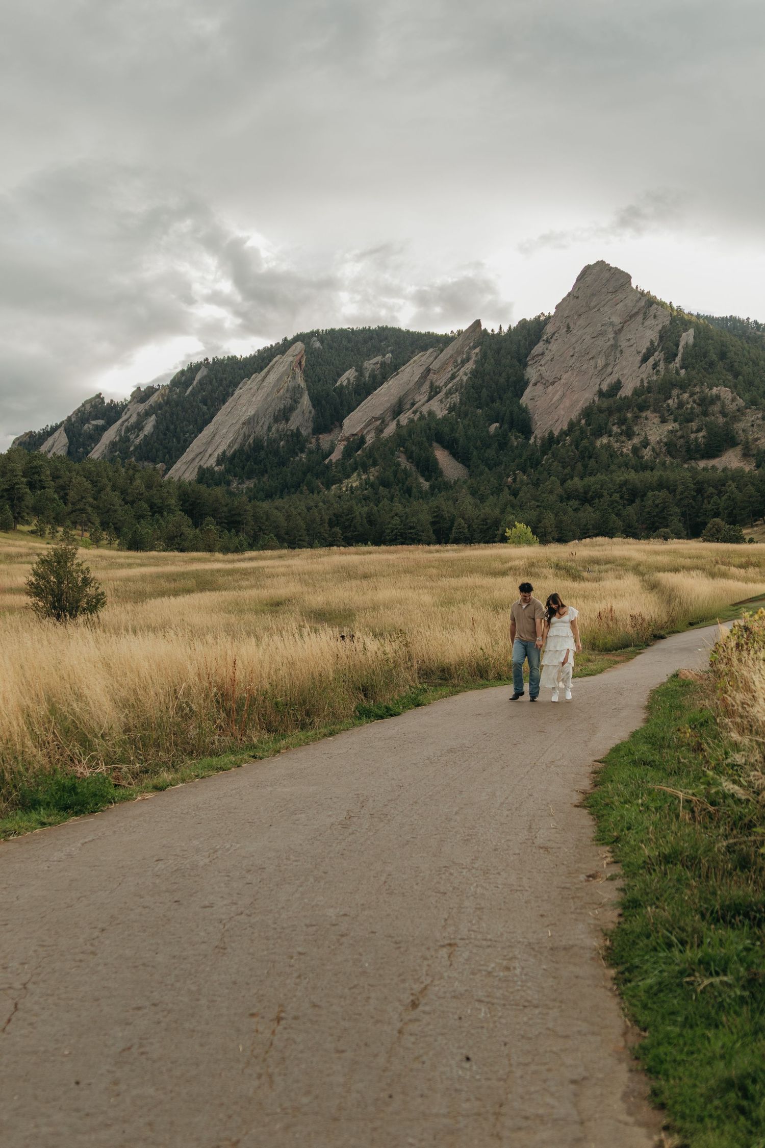 Couple walking hand in hand on path toward stunning Flatiron rock formations in Boulder Colorado.
