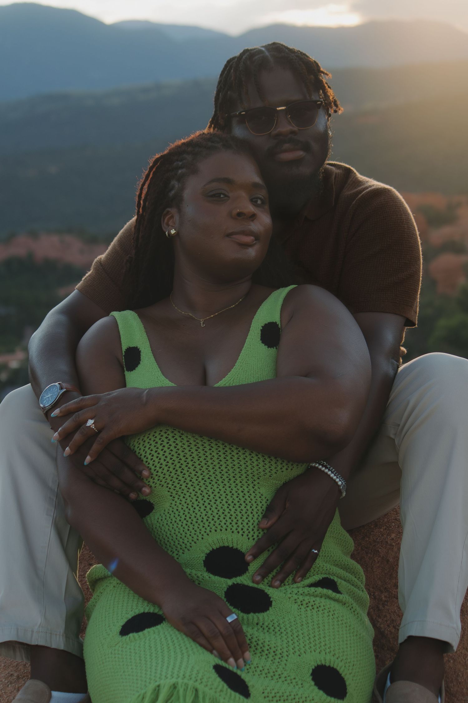 A couple embraces while sitting outdoors at sunset with mountains visible in the background.