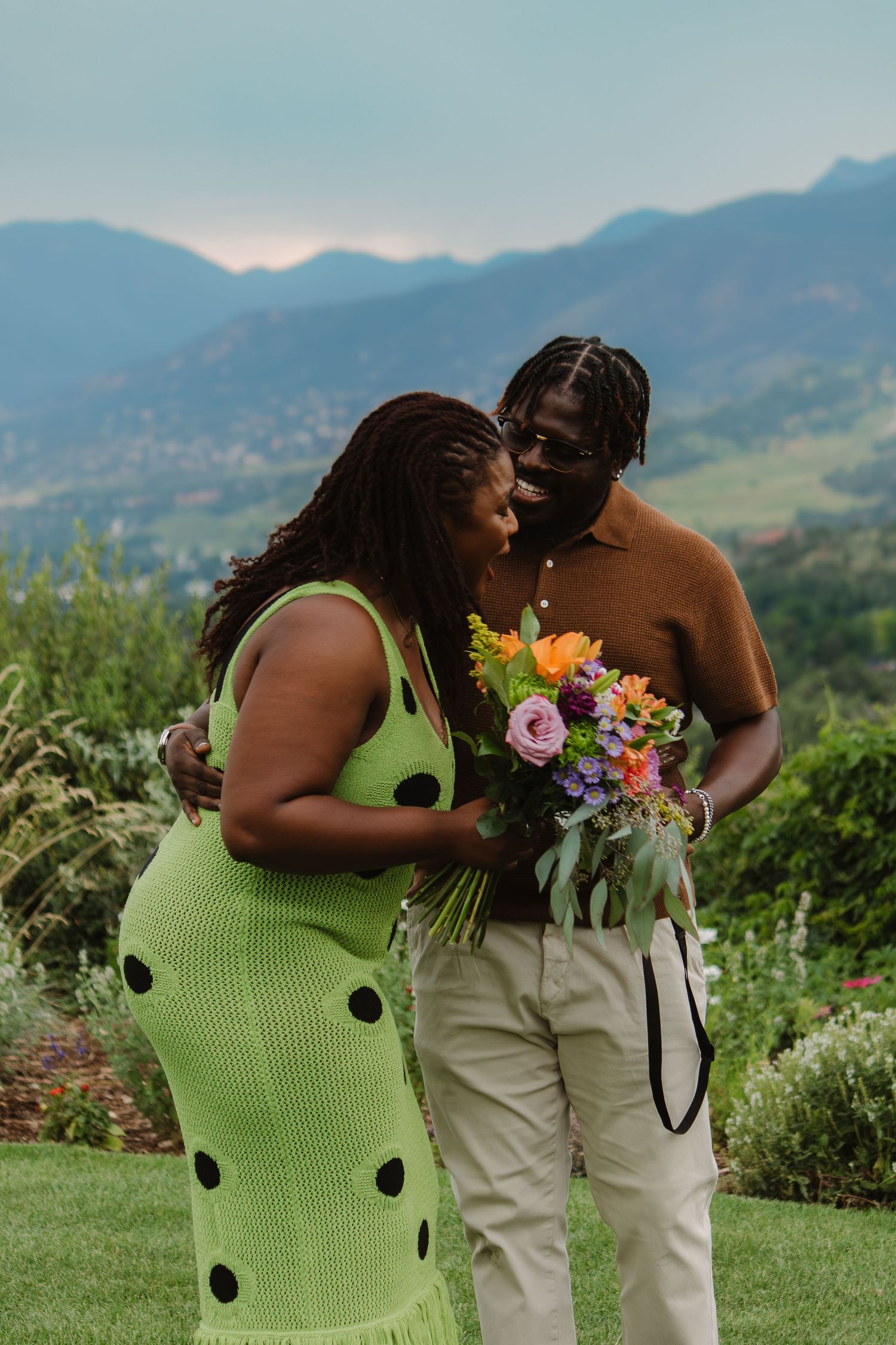 A couple shares an intimate moment in a mountain garden setting with a colorful bouquet of fresh flowers.