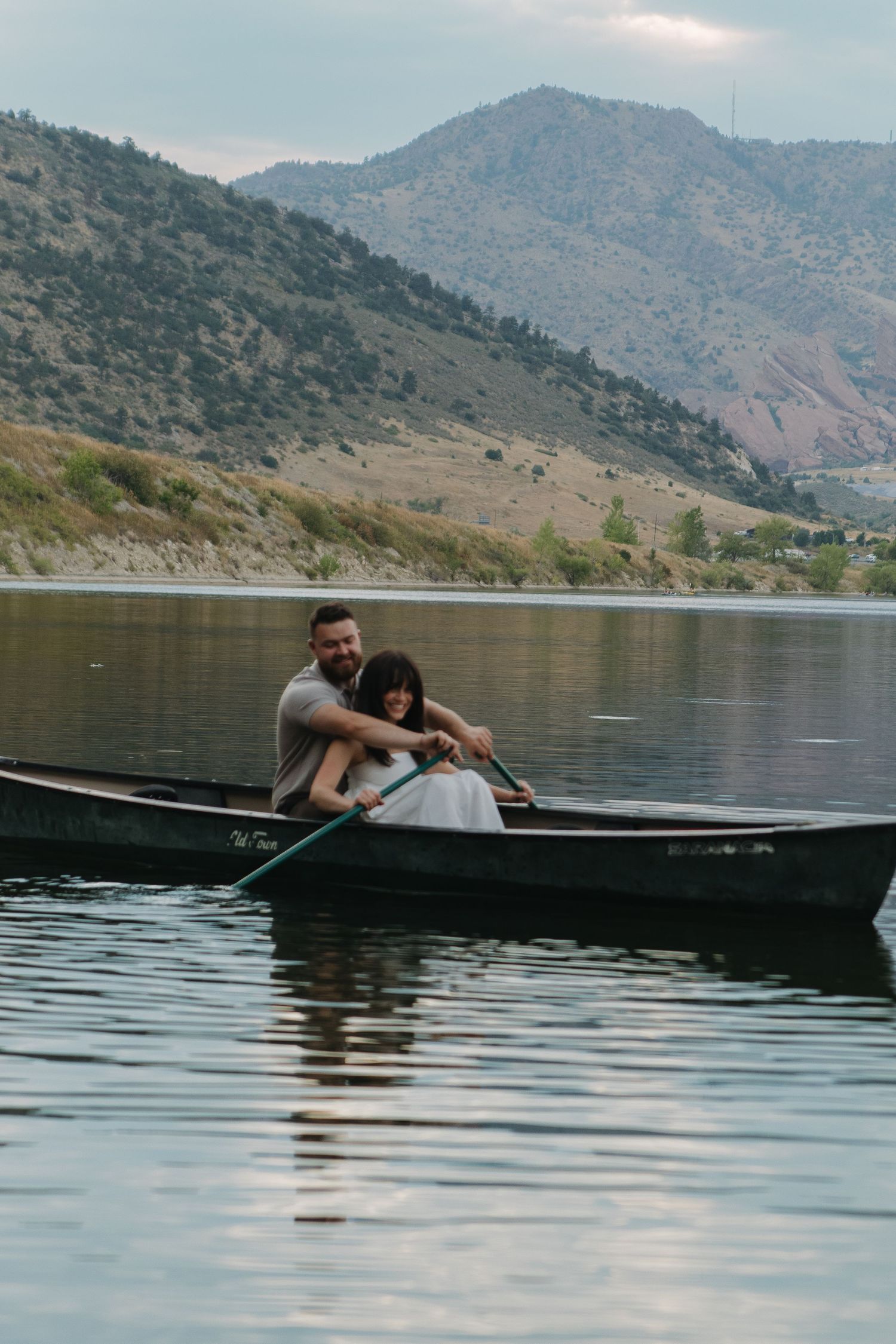 Couple cuddles while canoeing on mountain lake with scenic hills in background.