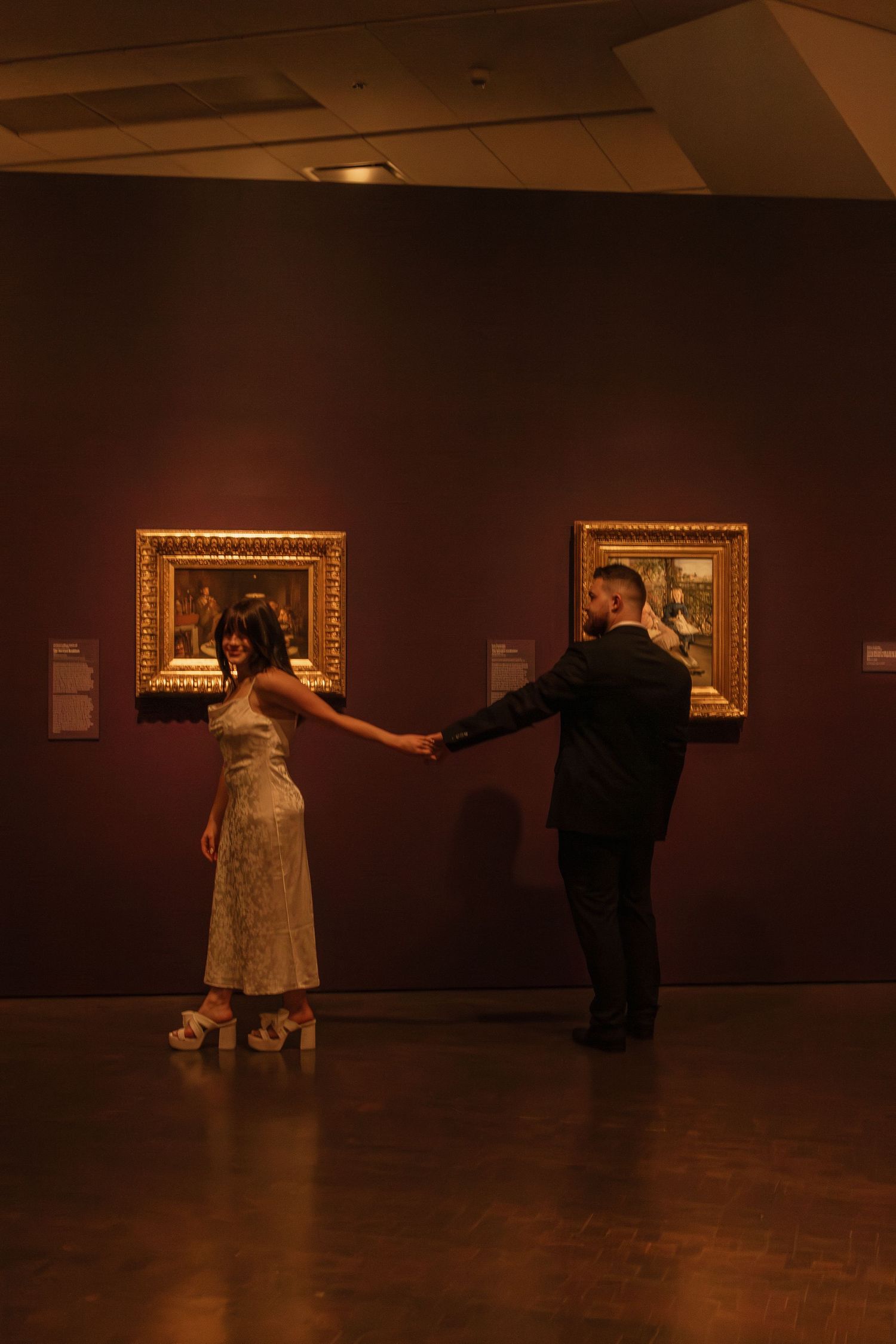 A couple dancing elegantly in a dimly lit art gallery surrounded by framed paintings.