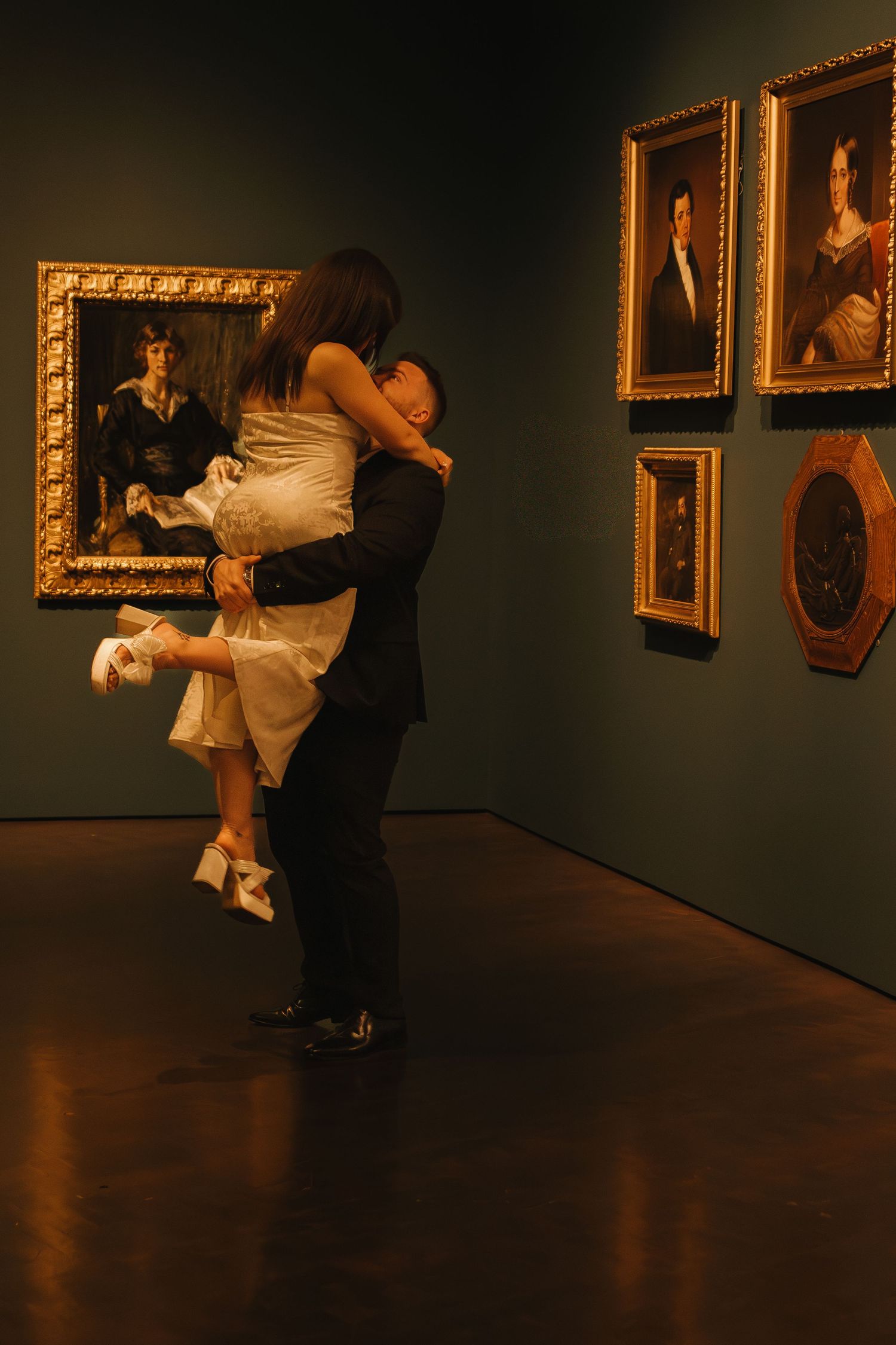 A couple performs a dramatic dance dip in an art gallery with golden frames on the wall.