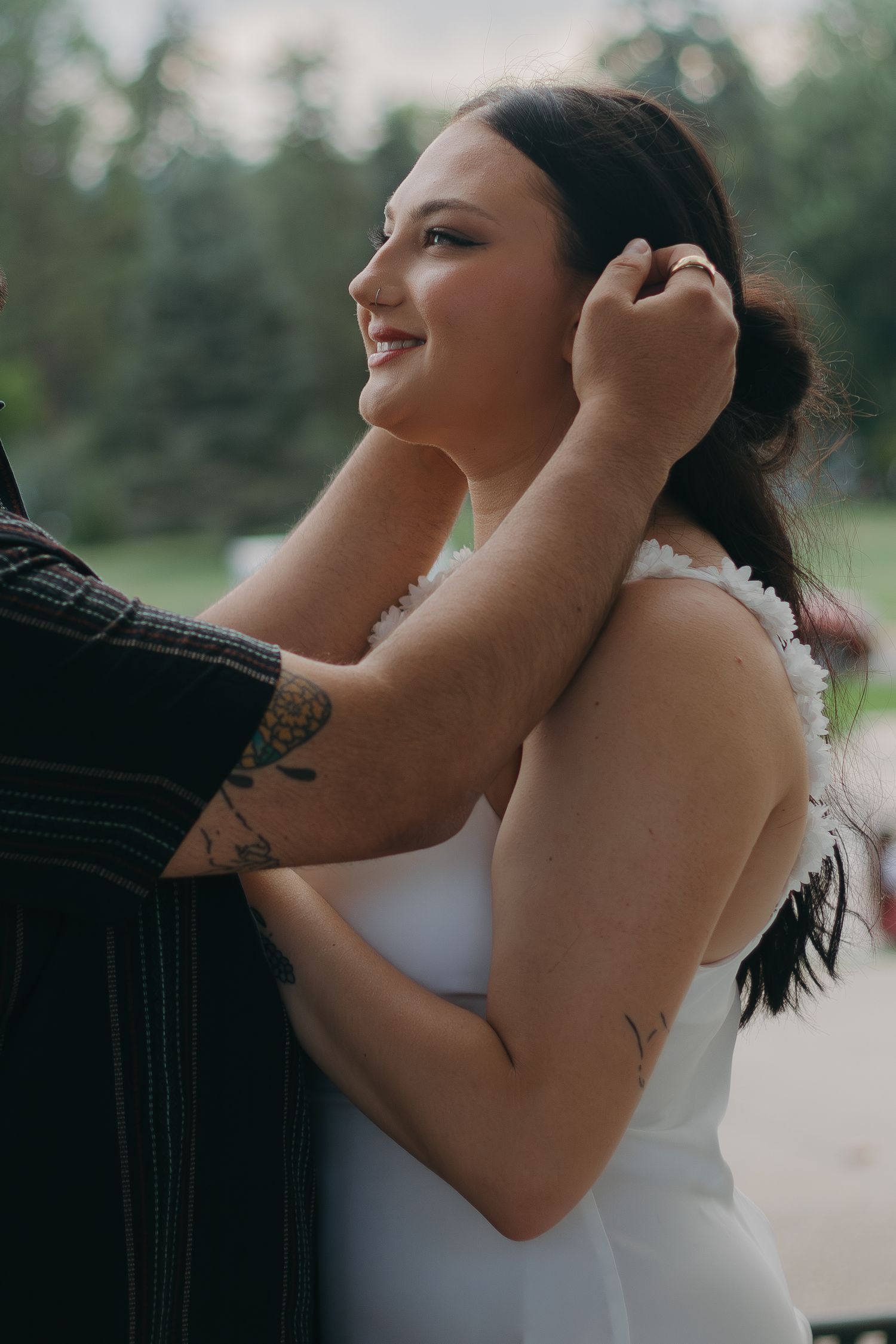 An intimate outdoor portrait showing a tender embrace against natural greenery.