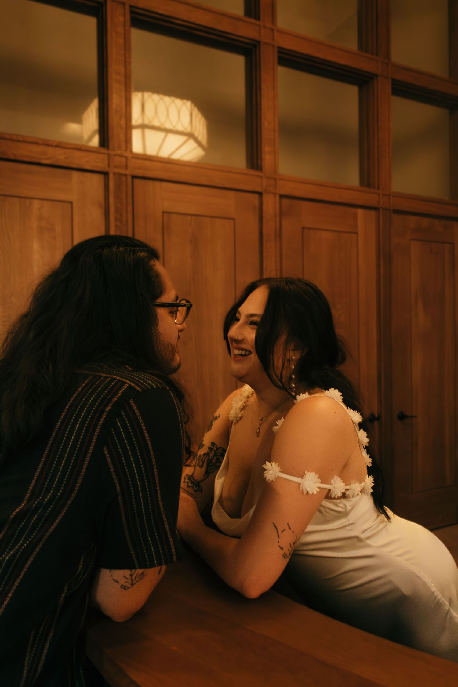 An intimate moment captured between a couple against wooden paneled walls with soft lighting.