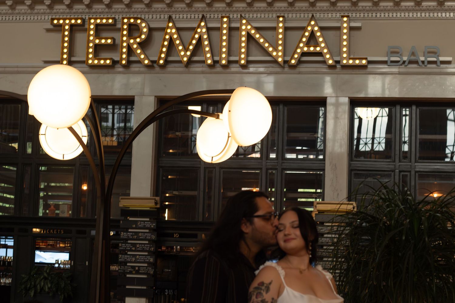 A romantic scene beneath the illuminated TERMINAL sign with glowing spherical light fixtures.