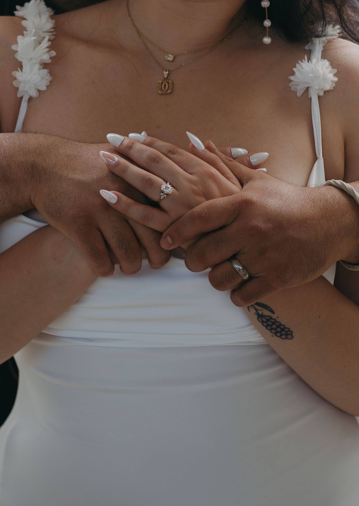 Close up of hands with wedding rings and white floral details showing an intimate moment.