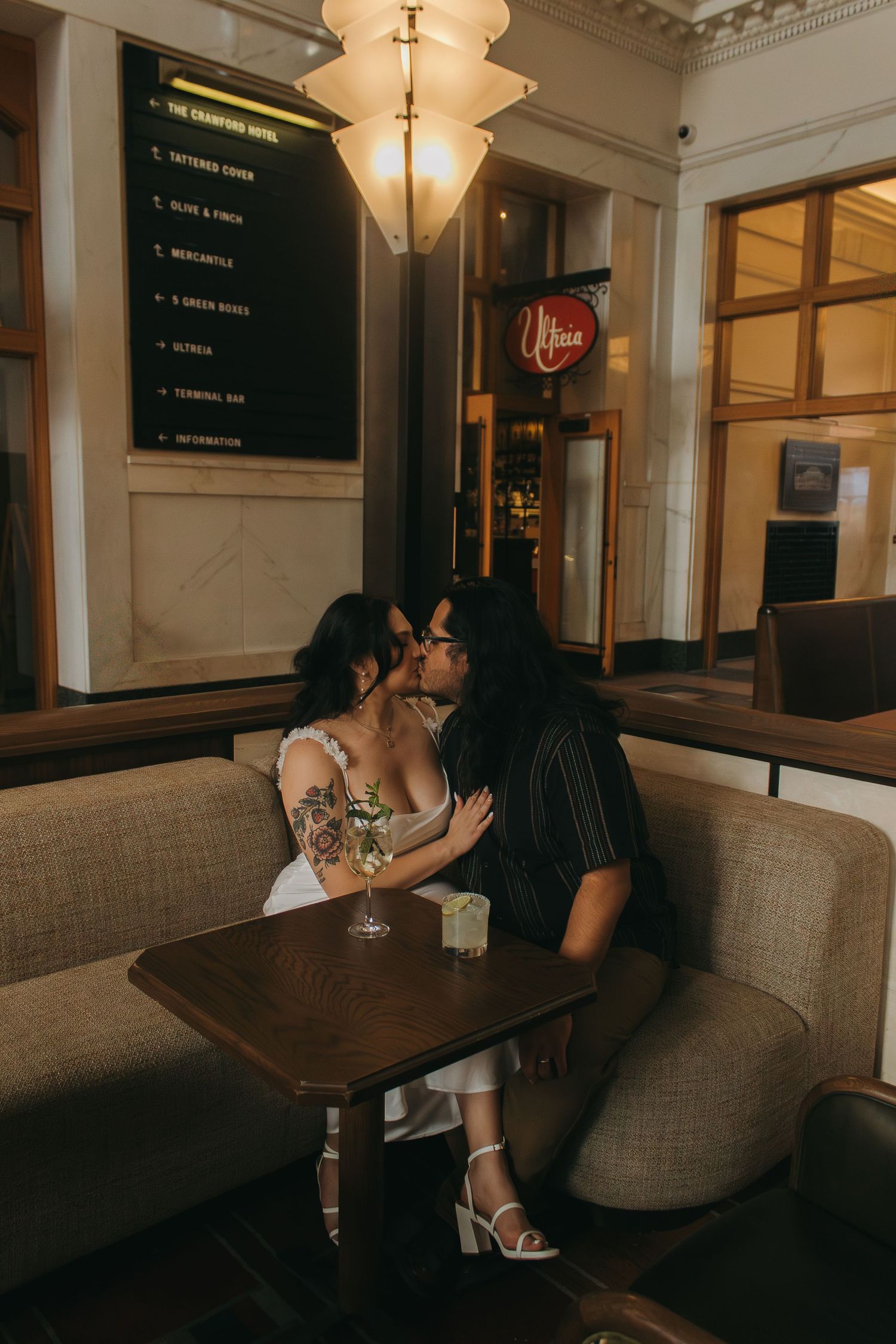 A romantic couple shares an intimate moment at a dimly lit restaurant booth with vintage decor and neon signage.