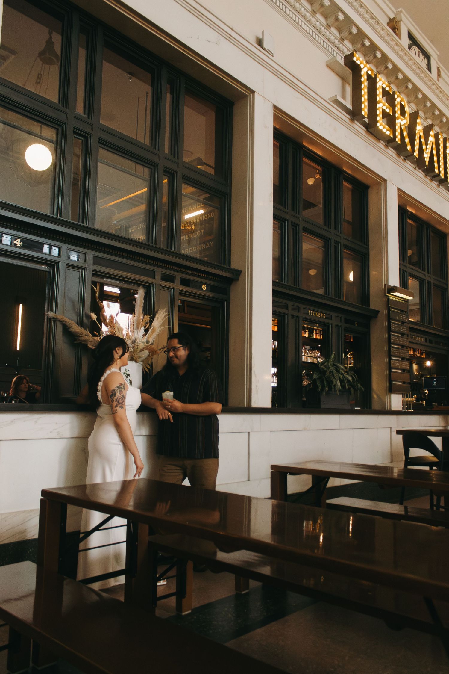 Romantic scenes unfold in an elegant restaurant with dark wooden benches and white walls.