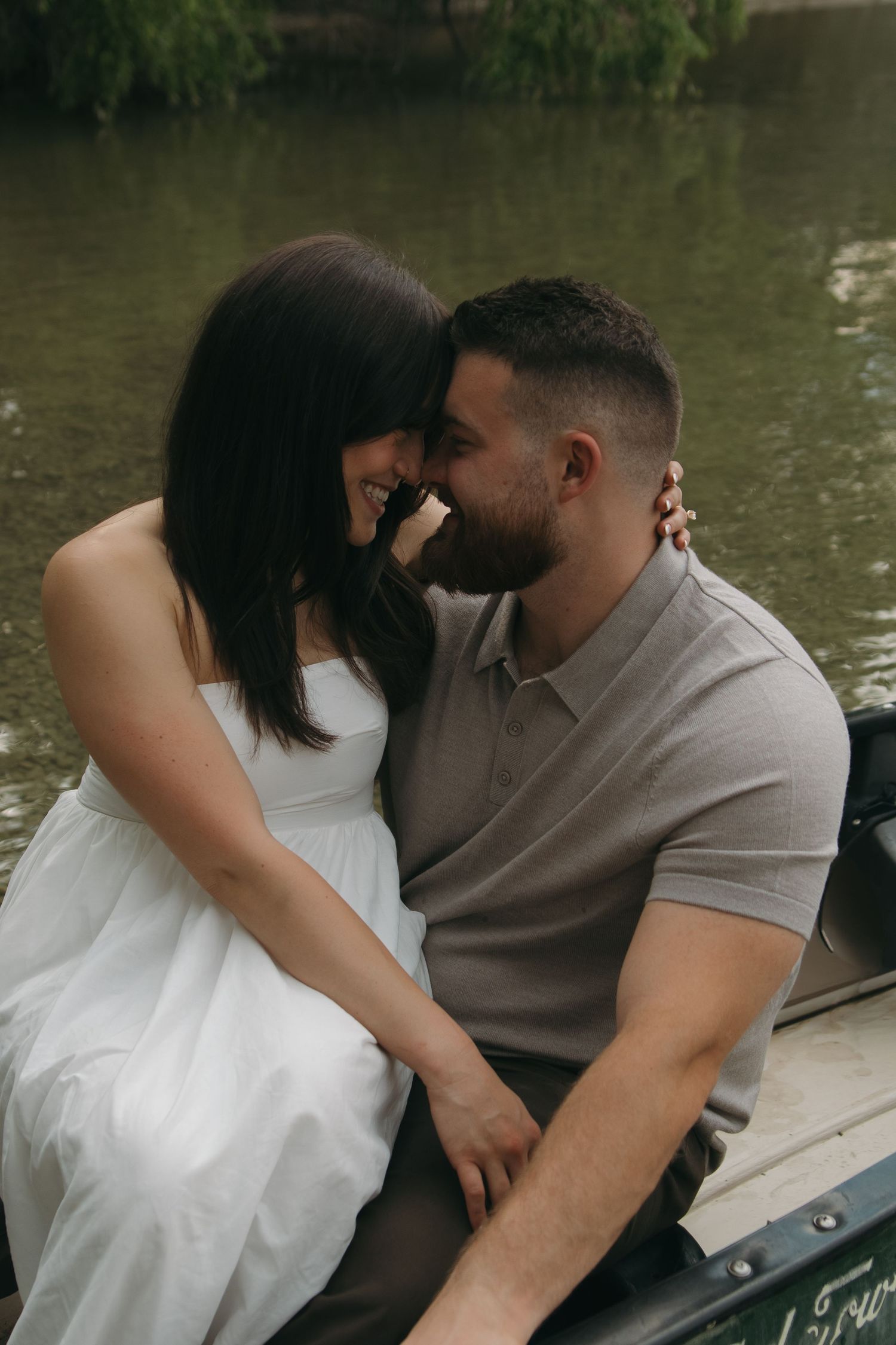 Two people share a close moment while sitting in a wooden boat on calm waters.
