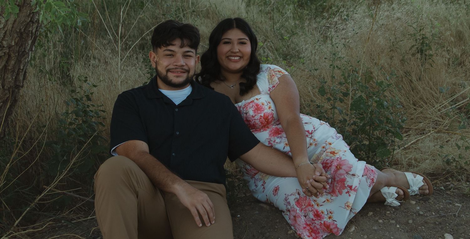 A couple sits together in a natural setting surrounded by greenery.