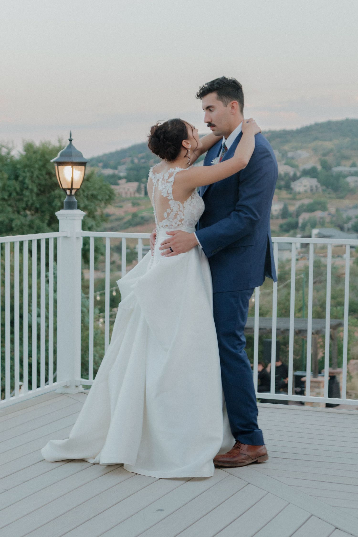 Newlyweds share intimate dance moments on white deck with mountain backdrop at sunset.