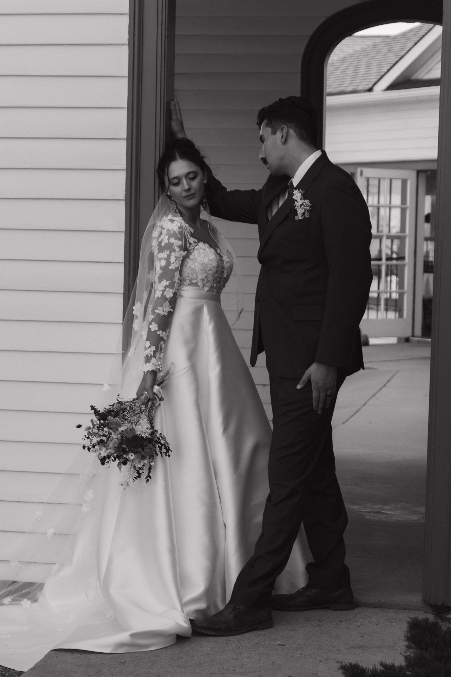 Black and white series showing wedding couple posing against white building exterior.