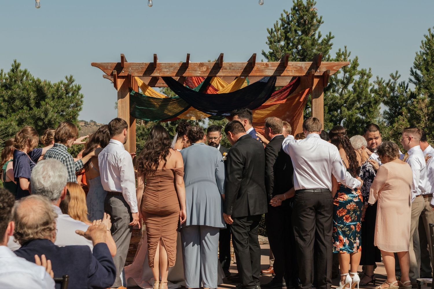 Large crowd of wedding guests with raised arms during outdoor ceremony in mountain setting.
