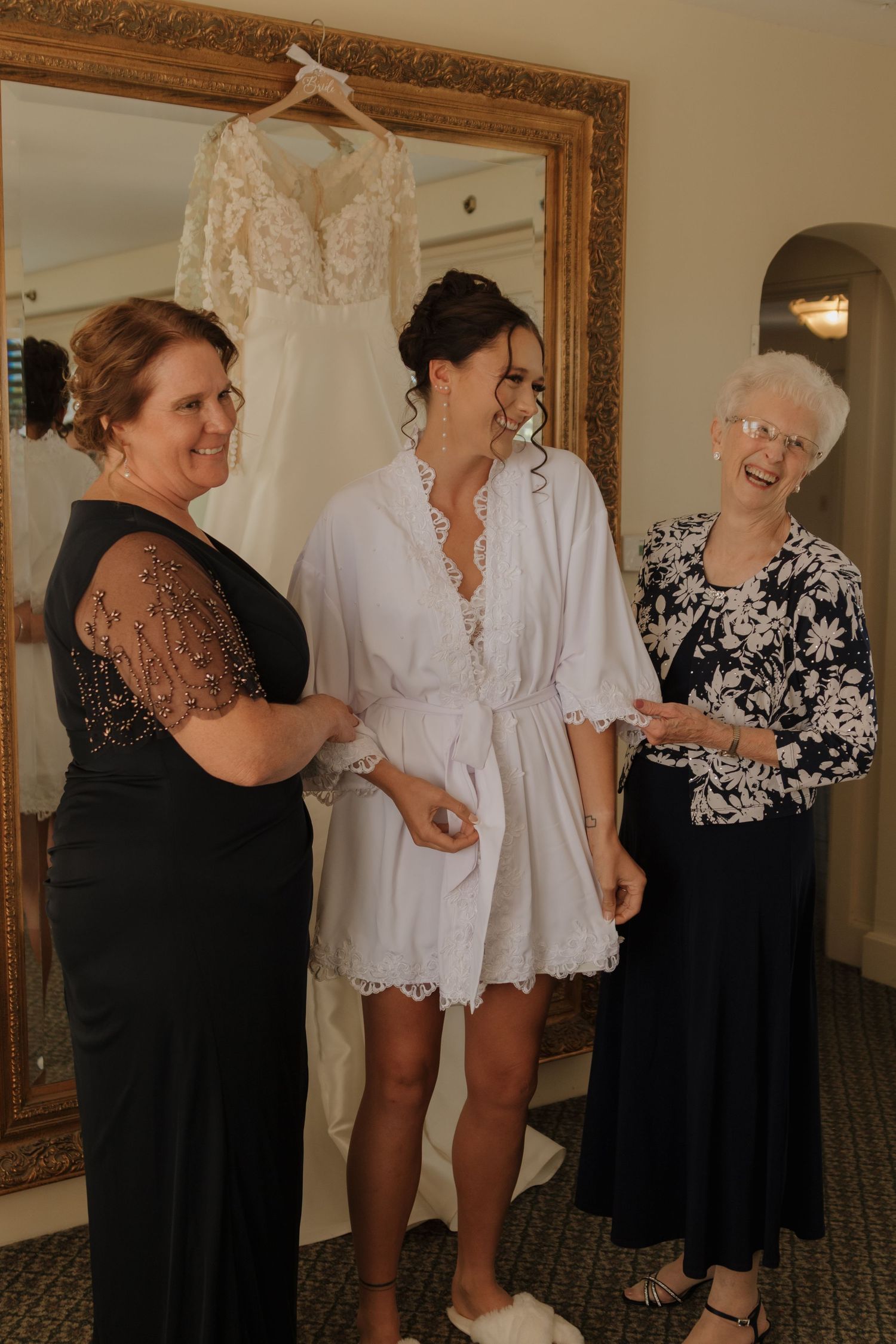 Women in black and white outfits sharing a joyful moment before a wedding.