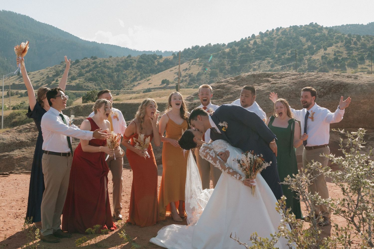 Wedding party and guests celebrating with raised arms against mountain vista.