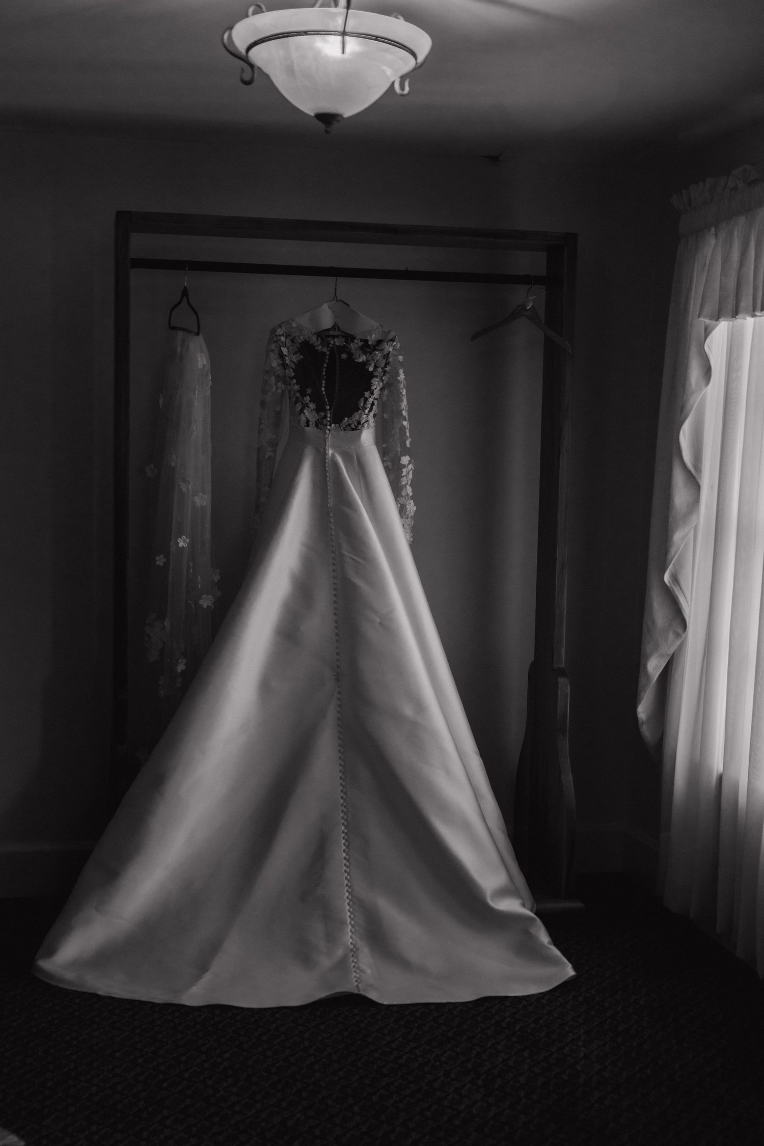 Multiple black and white photographs of a white wedding dress hanging against dark backgrounds with overhead lighting.