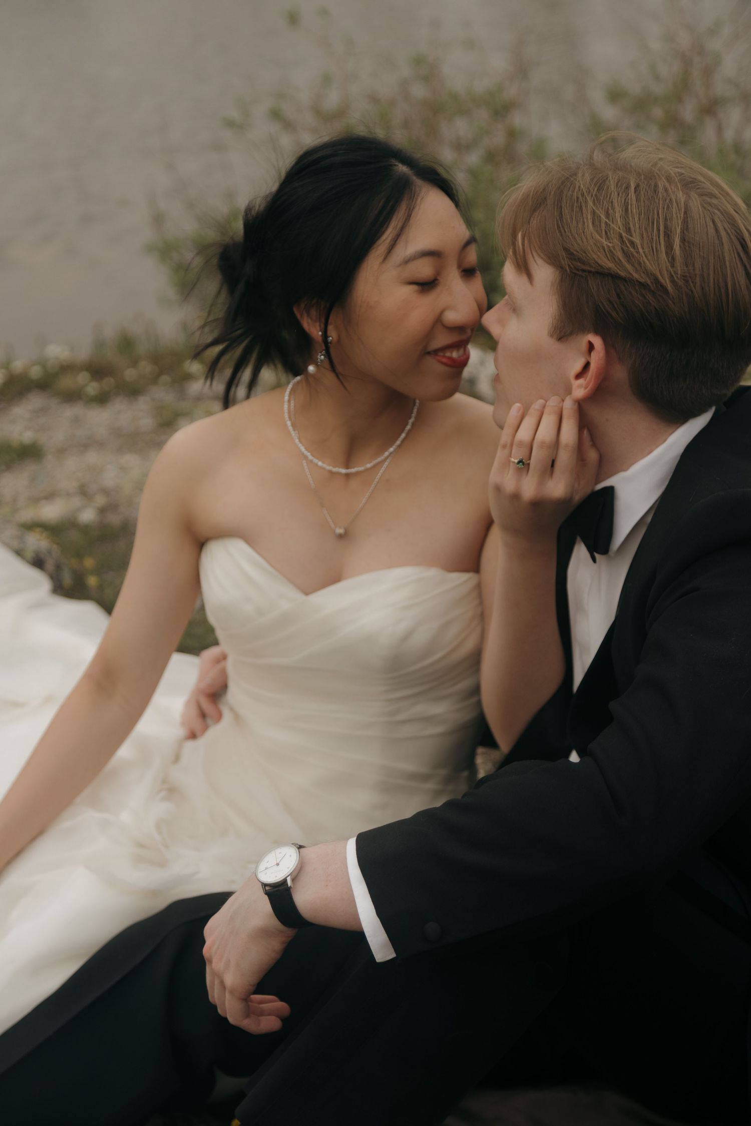 Bride in strapless white gown tenderly holds groom's face as they share an intimate moment while seated.