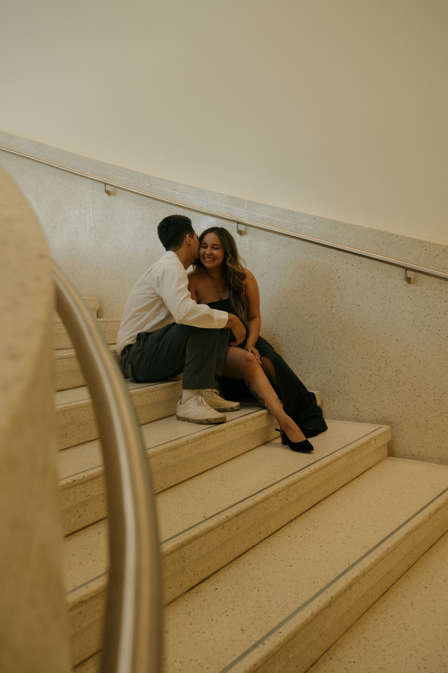 Couple sitting close together on marble stairs, sharing an intimate moment in a softly lit indoor setting.