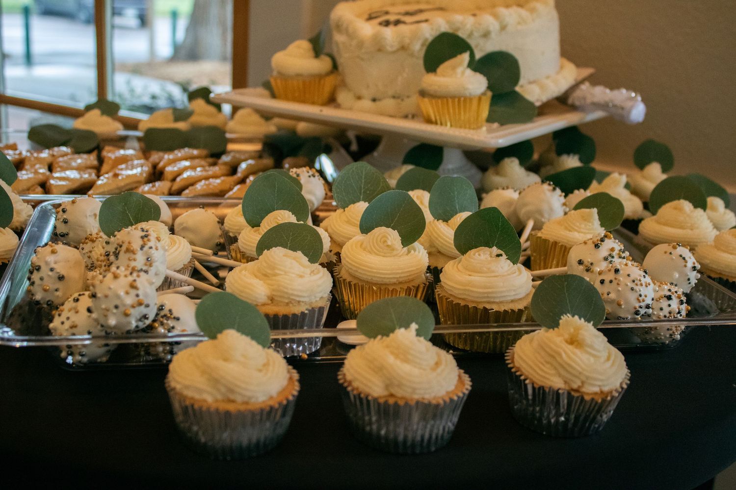 Display of wedding cupcakes with white frosting and green leaf decorations arranged on tiered stands.
