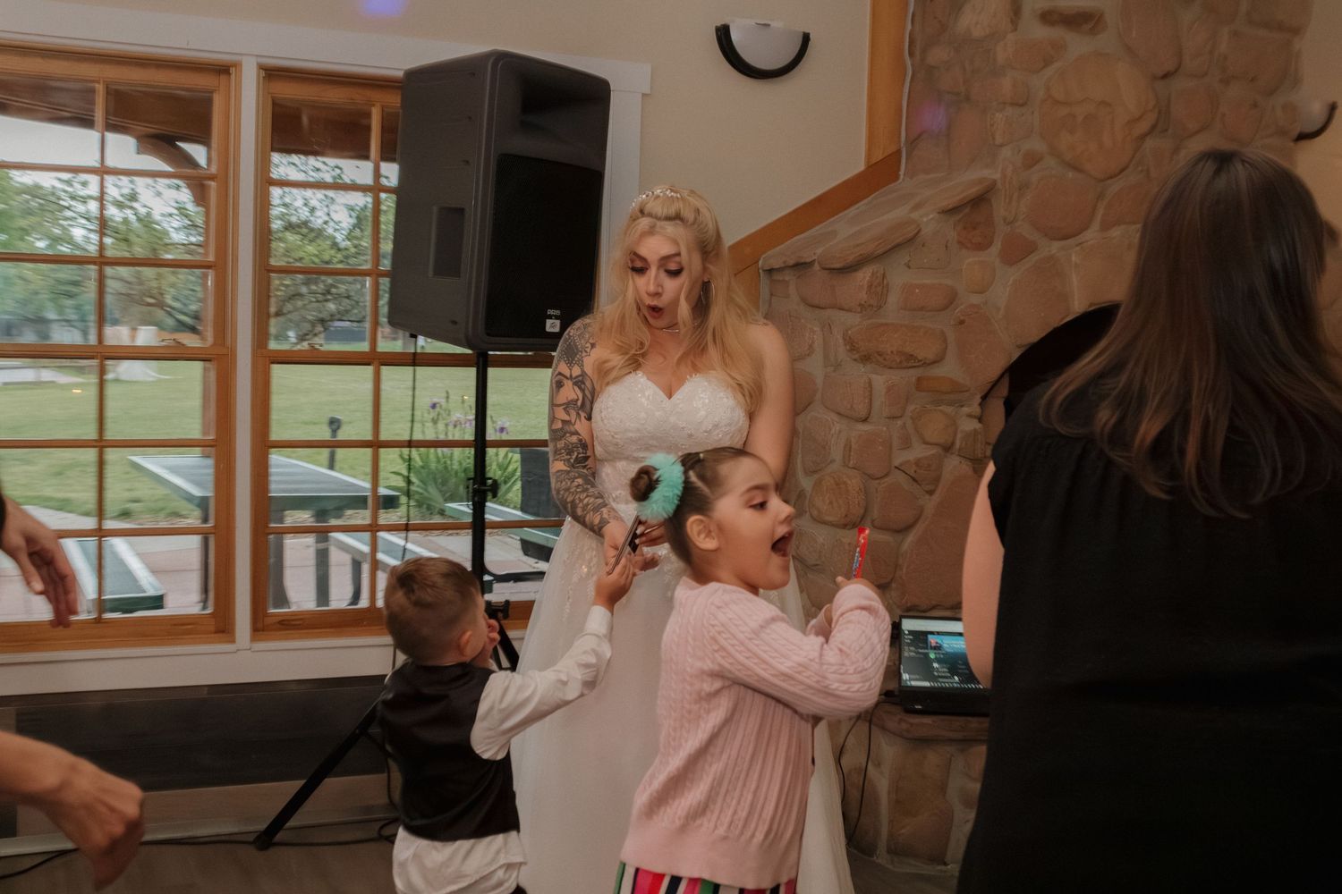 Wedding reception scene showing dancing and celebration with a stone fireplace in the background.