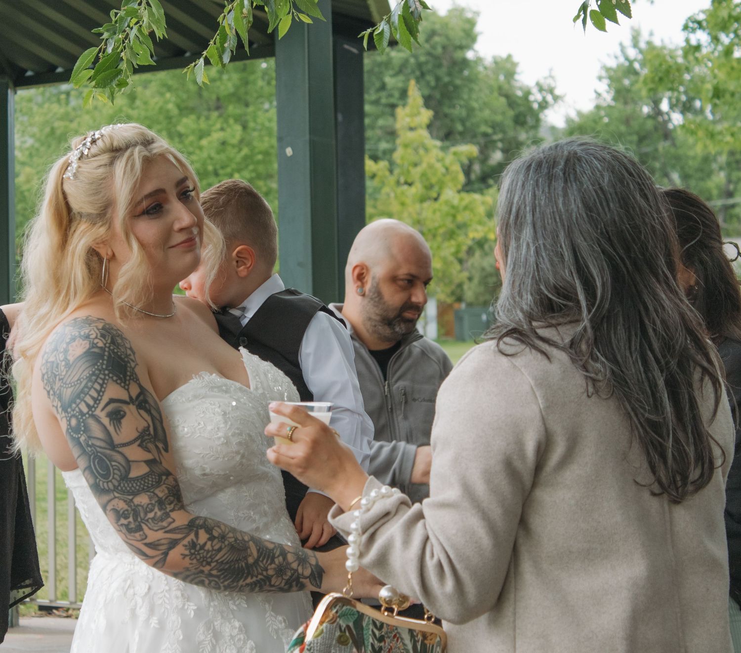 A bride with intricate tattoos participates in a wedding ceremony under a gazebo.