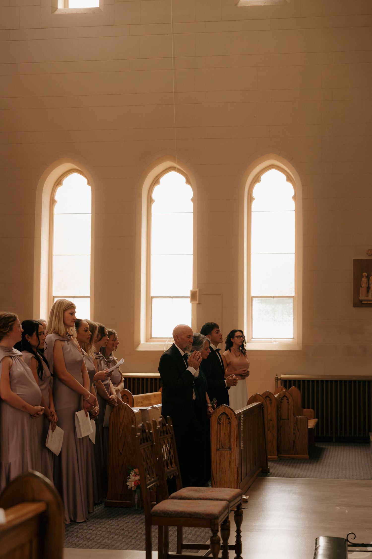 Wide angle black and white church interior showing bride walking down aisle with father past seated wedding guests.