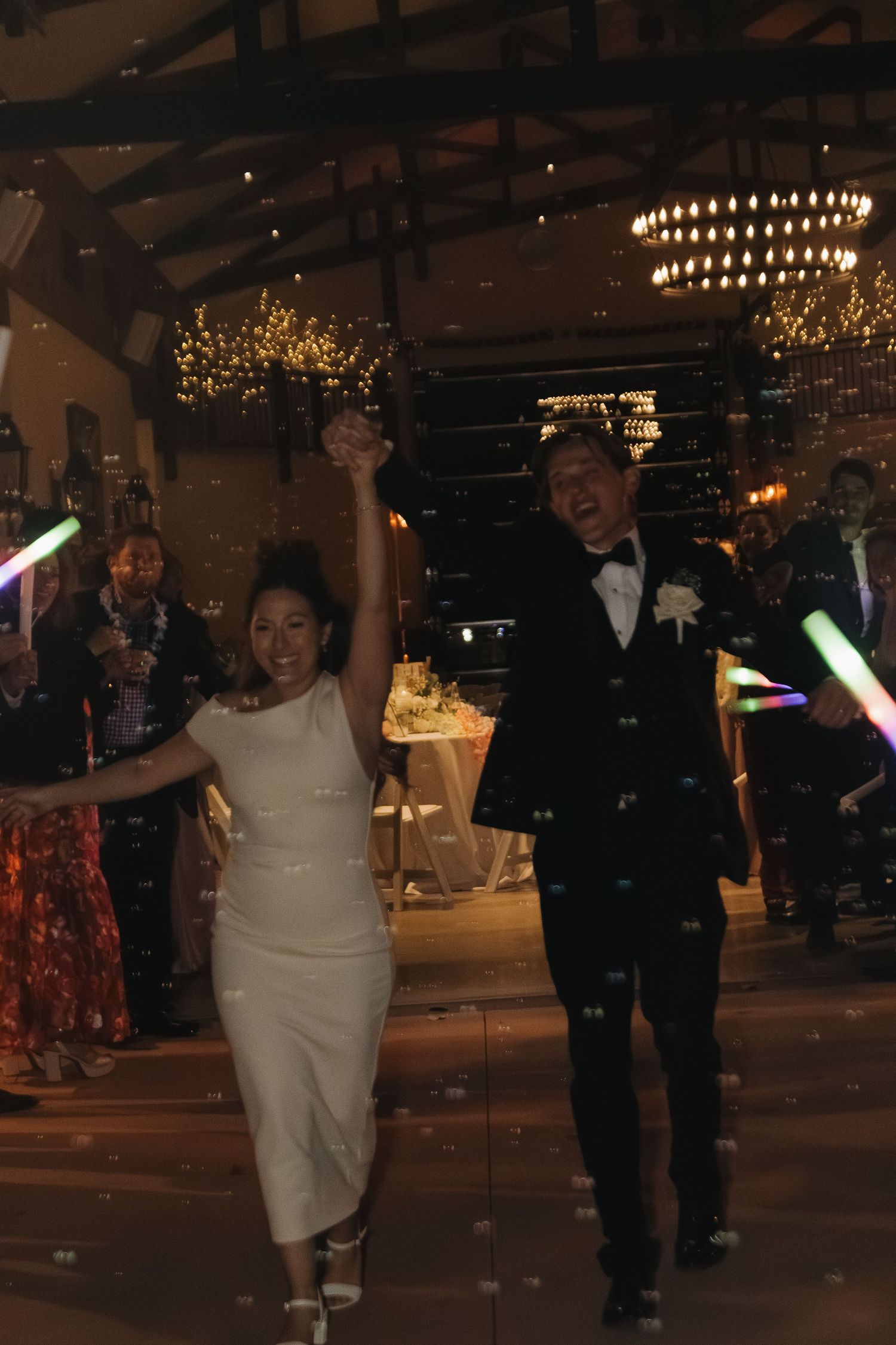 Wedding reception dance party with glowing light sabers and chandeliers in a rustic venue.