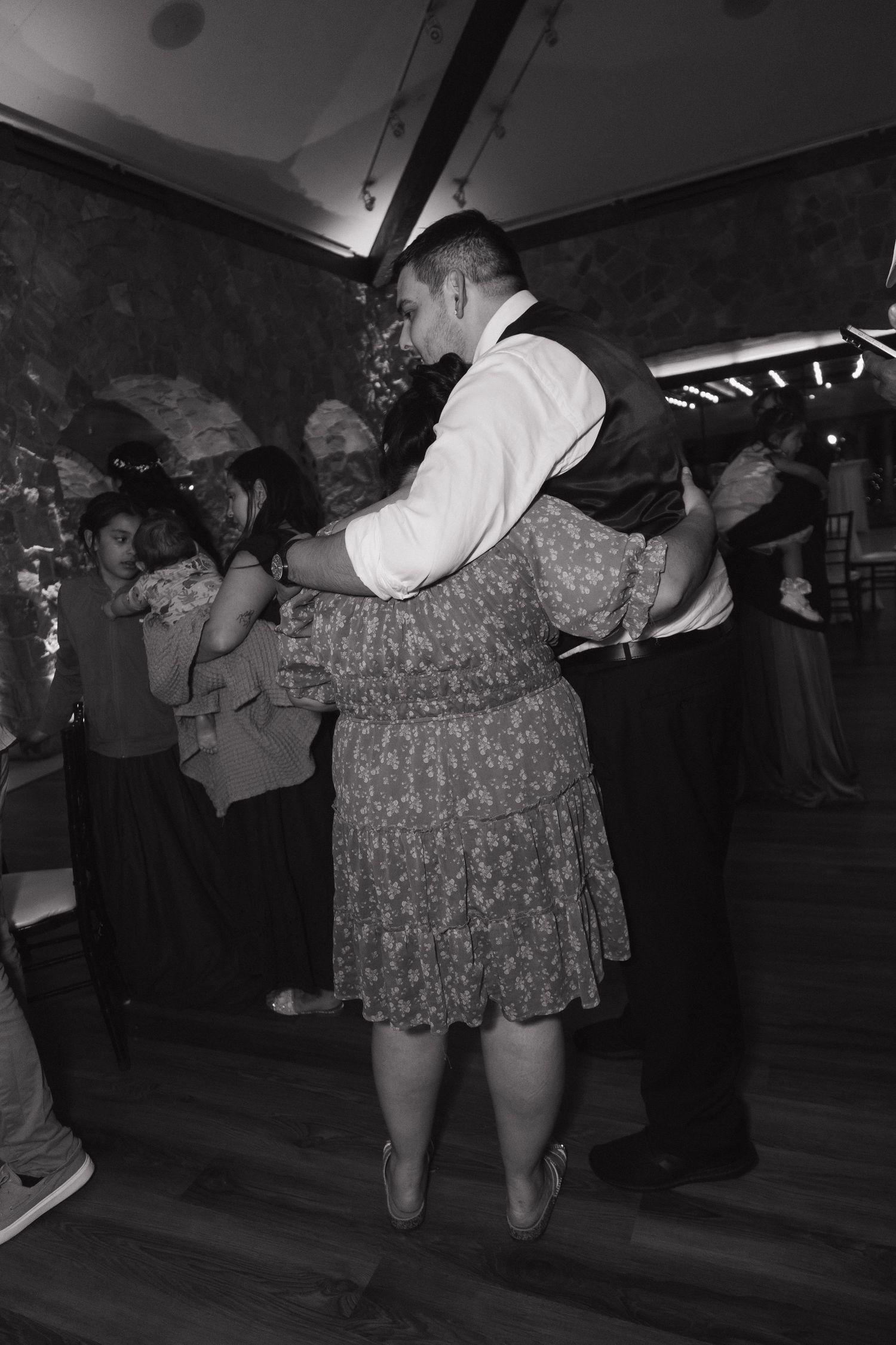 Black and white photo of couples dancing together at a lively wedding reception on a wooden dance floor.