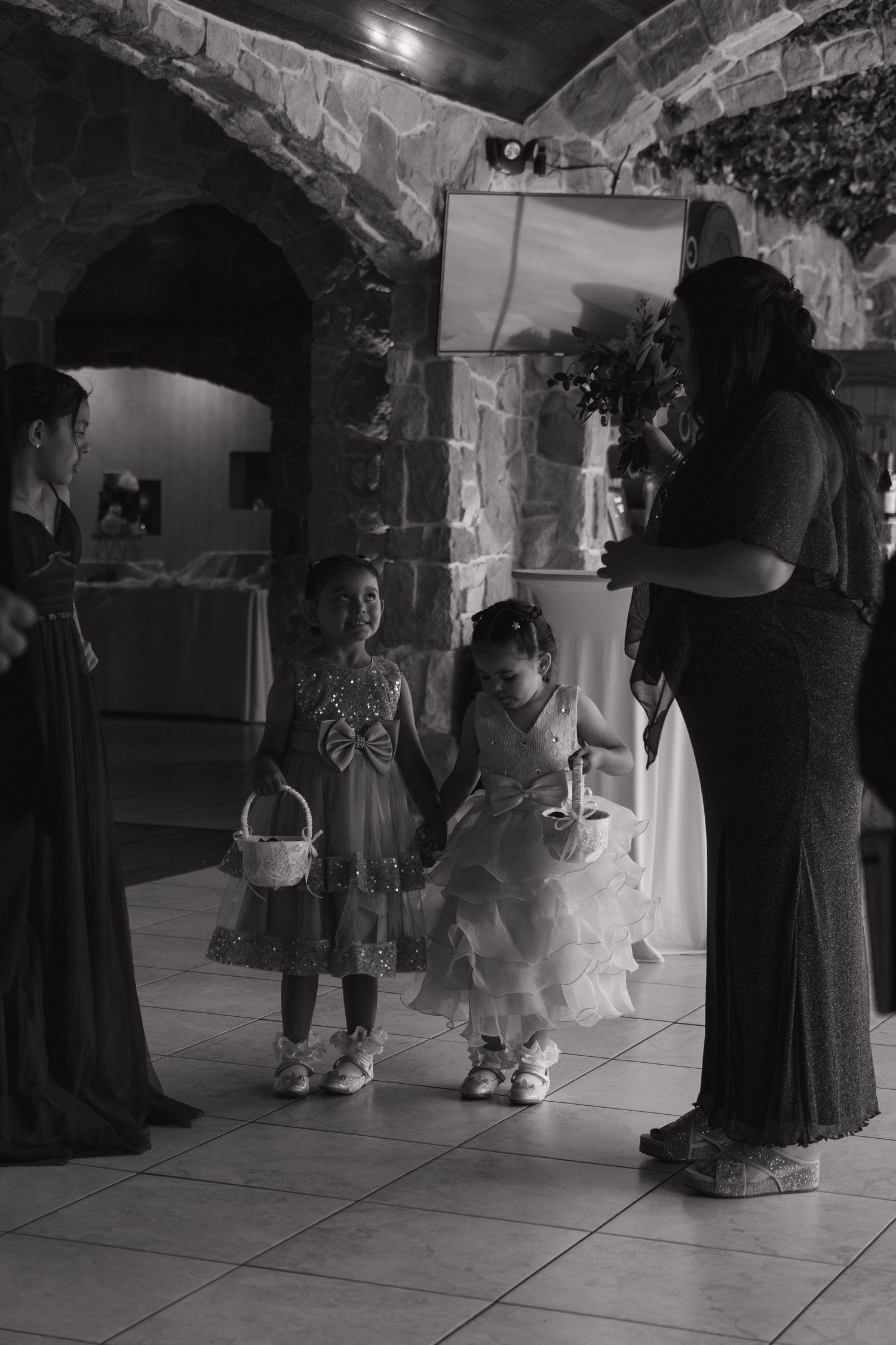 Black and white photo of two flower girls with baskets preparing to walk down the aisle at wedding ceremony.
